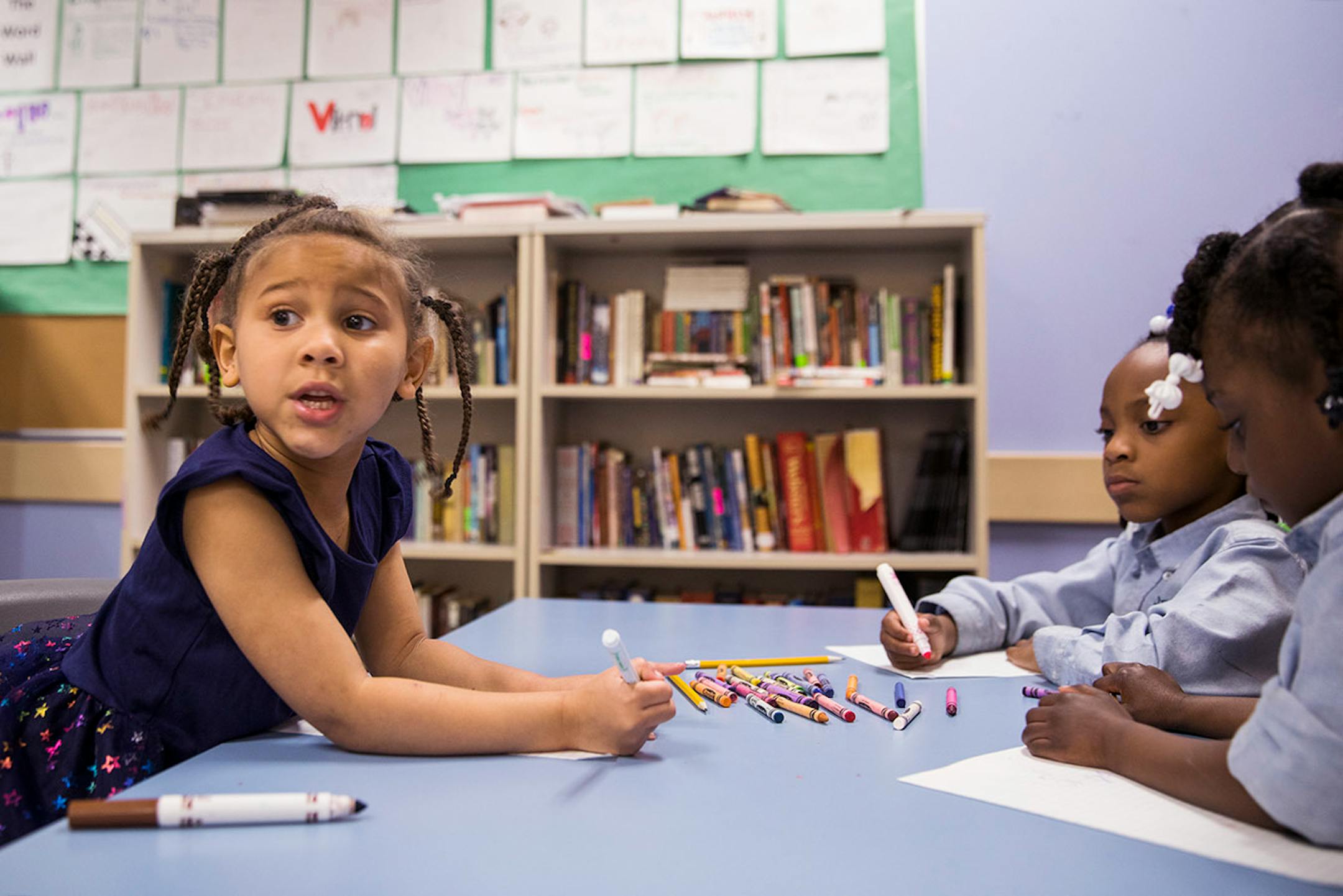Cayla Young, left, 5, looks at the board to write down a math problem during after school programing.