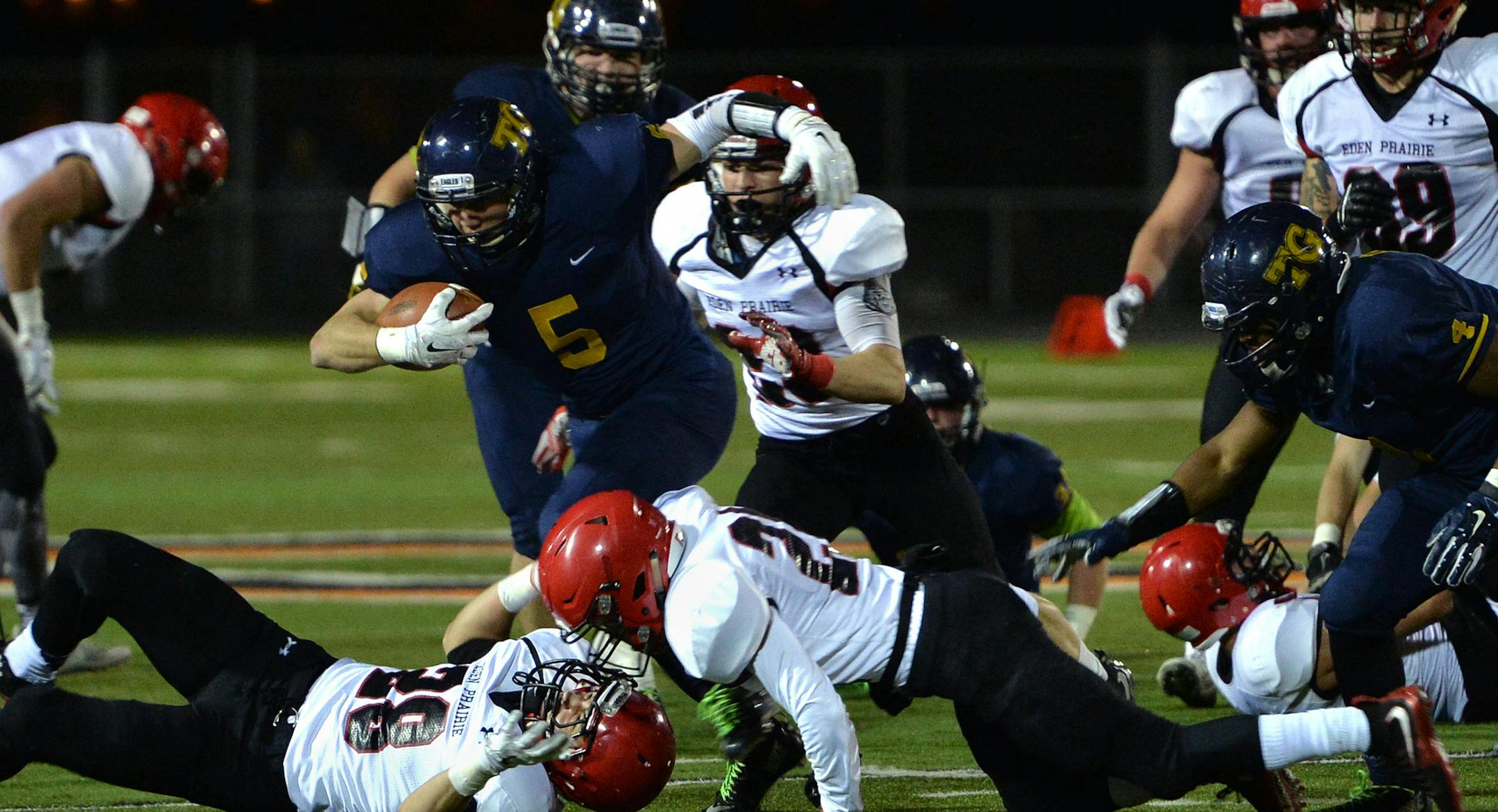 Totino-Grace junior Ivan Burlak carries the ball through Eden Prairie defense during the first half of the Class 6A state tournament quarterfinal game Friday night at Osseo High School. Eden Prairie led Totino-Grace 7-0 at halftime. ] (SPECIAL TO THE STAR TRIBUNE/BRE McGEE) **Ivan Burlak (blue, 5)