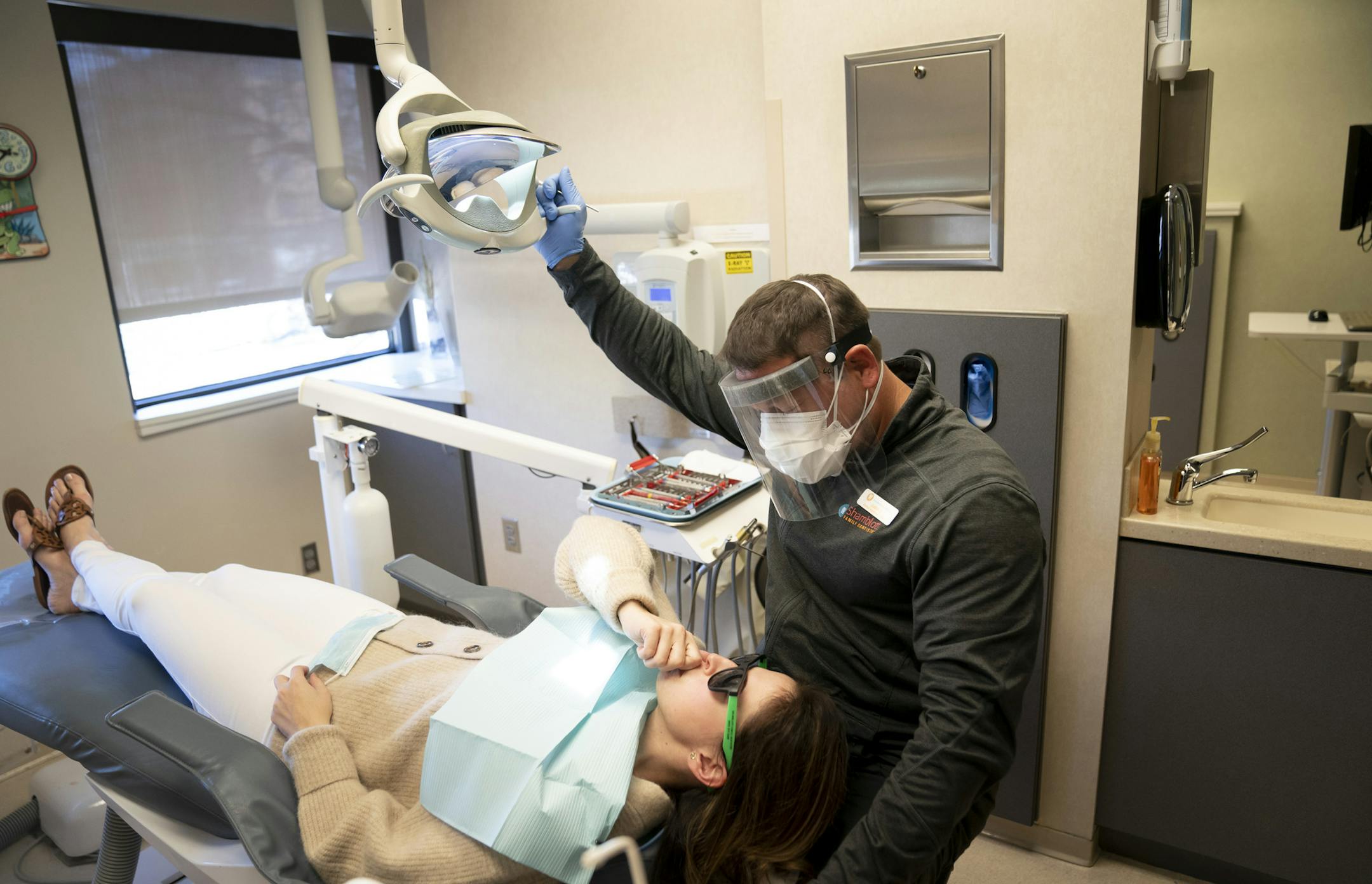 Dental hygienist Justin Jewison chatted with patient Stacy Ericson before her teeth cleaning at Shamblott Family Dentistry in Hopkins, Minn., on Tuesday, May 12, 2020. ] RENEE JONES SCHNEIDER ¥ renee.jones@startribune.com Shamblott Family Dentistry is taking extreme precaution as it opens back after the Covid-19 shutdown by double masking the doctors and hygienists, wearing plastic shields, taking customers temperatures when they arrive and having them sign a waiver that they don't have any risk