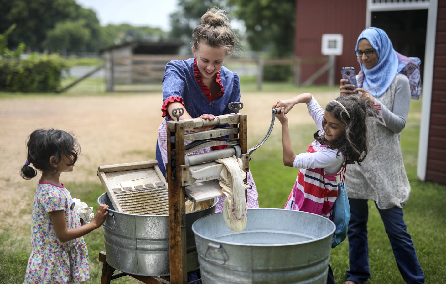 Eidem Farm, a historical homestead in Brooklyn Park, will likely get the go ahead from the city to start an $8.5 million master renovation plan. Here, Jennifer Cvek (center) dressed in period clothing, helps sisters Saara, (left) and Aasiya Bashir, 4 and 8, wash cloths with an old wash board and ringer. Mehtab Walj takes their picture at right. ] BRIAN PETERSON &#x2022; brian.peterson@startribune.com
Brooklyn Park, MN 07/11/2018