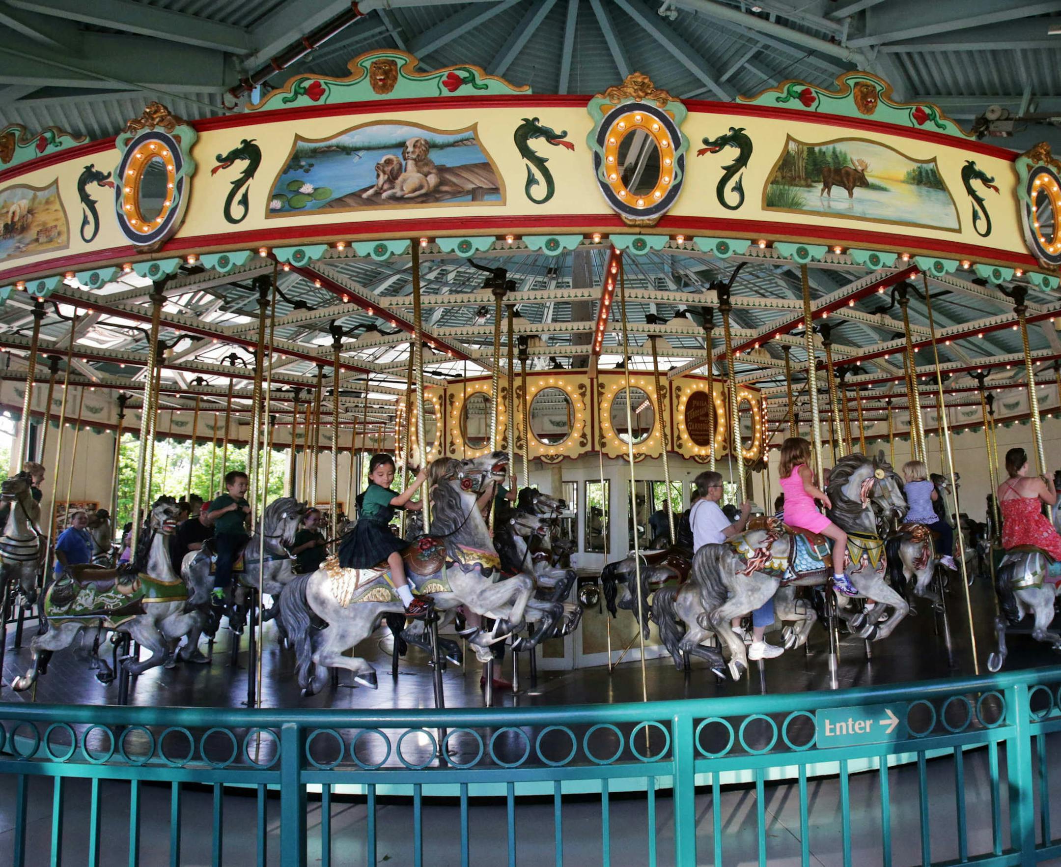In this photo taken Tuesday, June 3, 2014, visitors to the Como Town amusement park ride on the 100-year-old Cafesjian's Carousel in St. Paul, Minn. Parking at the Como Town and adjacent Como Park Zoo and Conservatory is free but there is a charge to ride the Carousel. (AP Photo/Jim Mone)