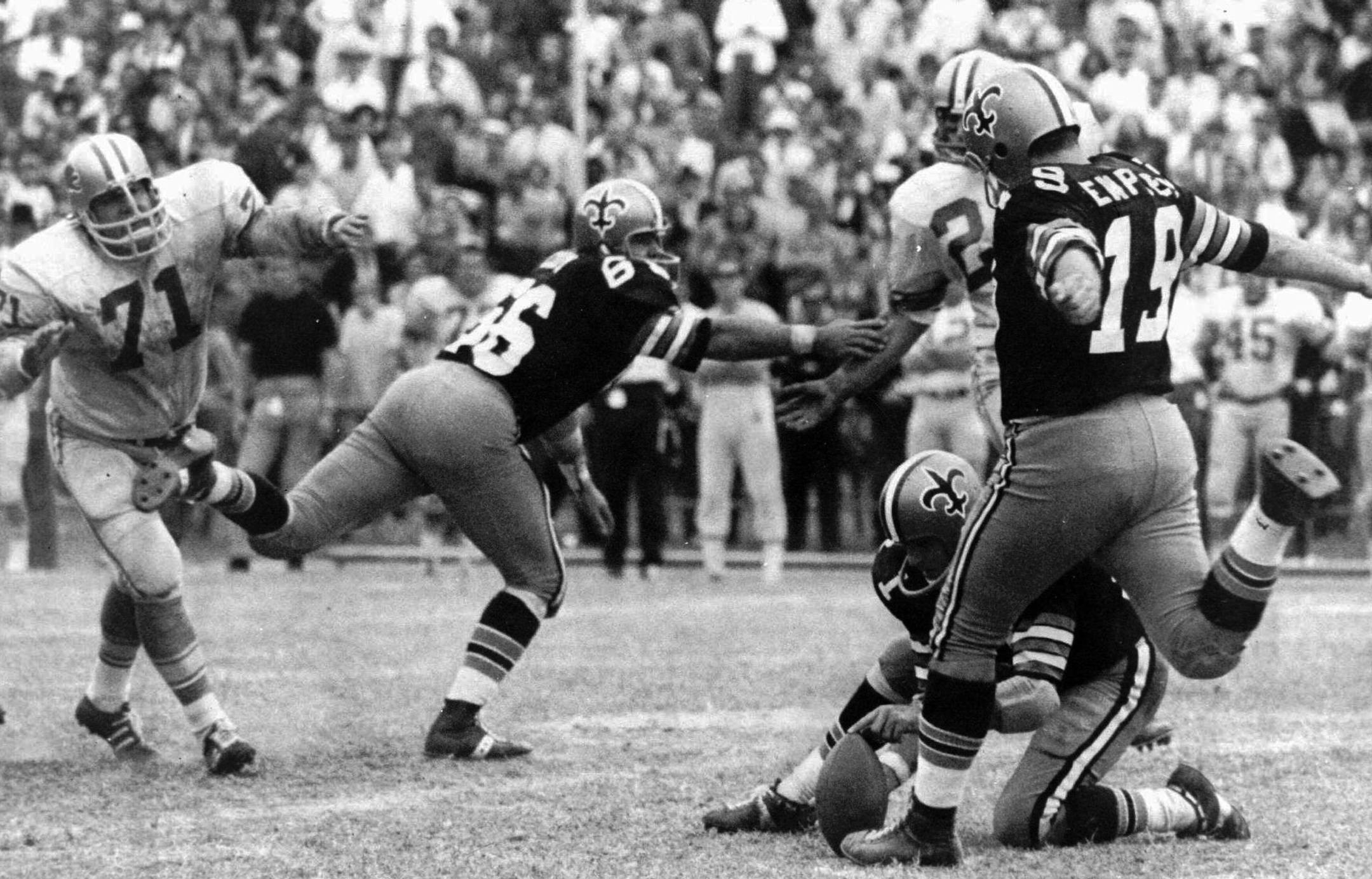 FILE - In this Nov. 8, 1970, file photo, New Orleans Saints' Tom Dempsey (19) moves up to kick a 63-yard field goal as teammate Joe Scarpati holds the ball and Detroit Lions' Alex Karras (71) rushes in while Saints' Bill Cody (66) blocks, in New Orleans. Dempsey, who played in the NFL despite being born without toes on his kicking foot and made a record 63-yard field goal, died late Saturday, April 4, 2020, in New Orleans while struggling with complications from the new coronavirus, his daughter