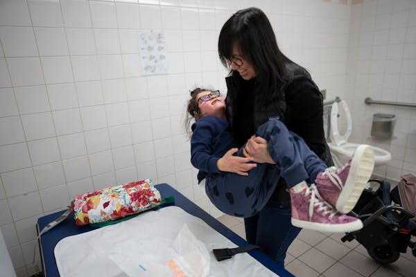 Tram Nguyen carries her daughter Sadie Sava, 7, from her wheelchair to an adult changing table in a family bathroom at the Mall of America in Blooming