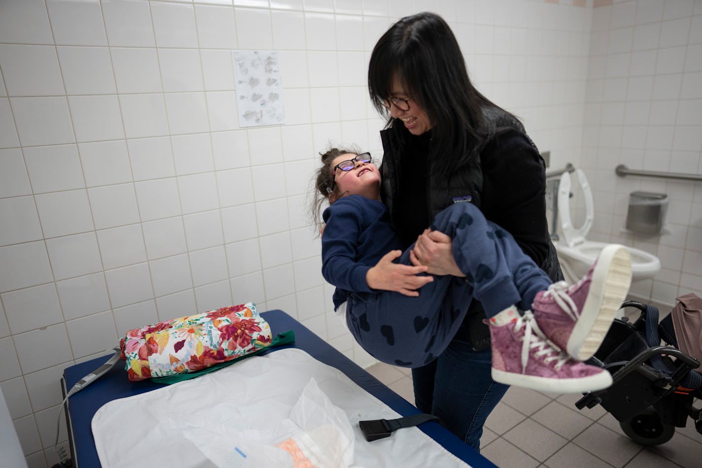 Tram Nguyen carries her daughter Sadie Sava, 7, from her wheelchair to an adult changing table in a family bathroom at the Mall of America in Bloomington, Minn., on Wednesday, March 15, 2023. ] RENEE JONES SCHNEIDER • renee.jones@startribune.com