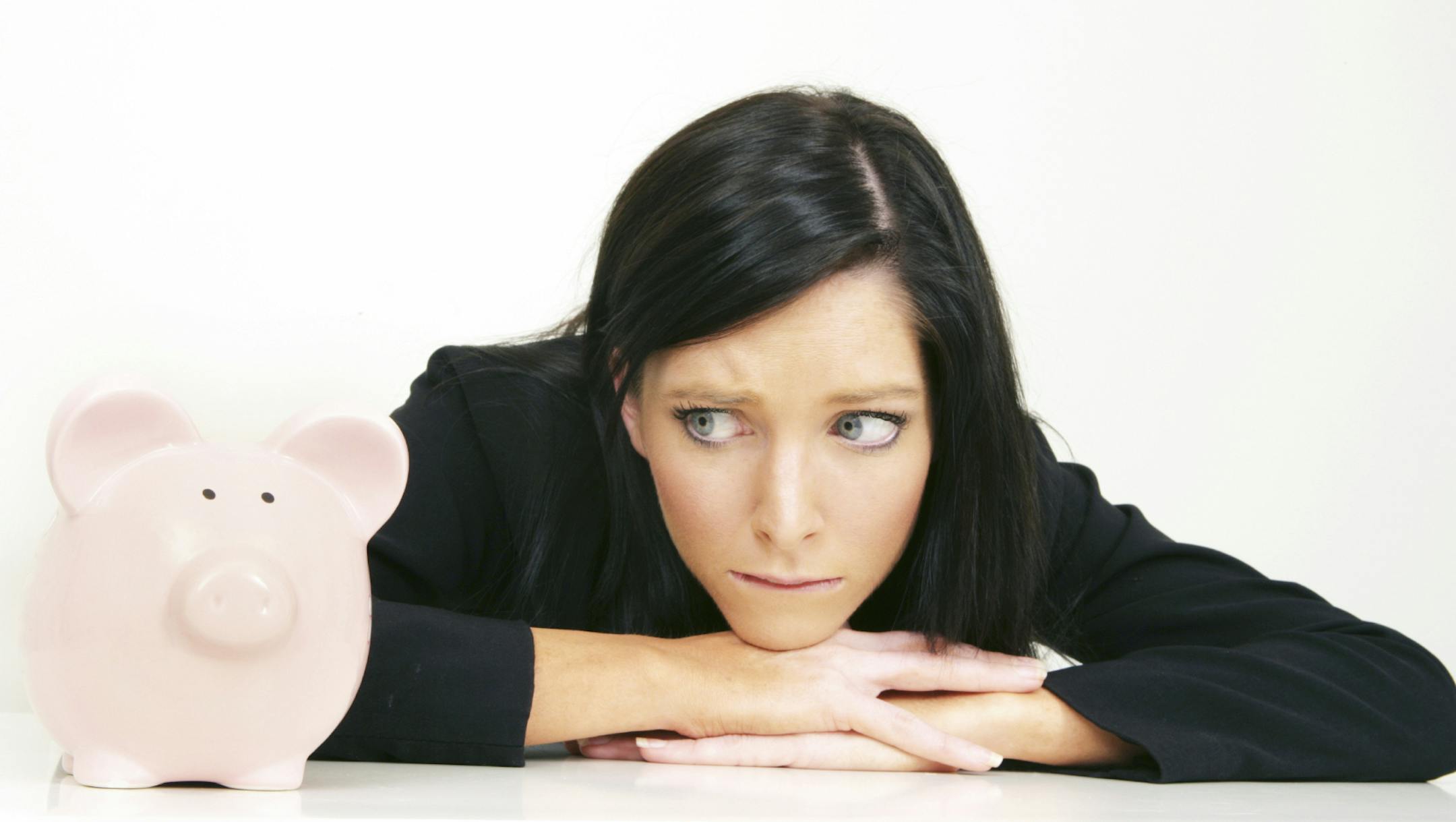 A woman looks worriedly at her piggy bank