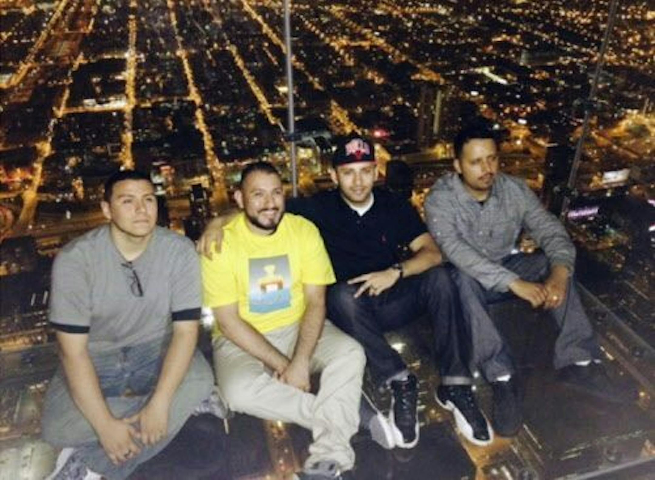This Wednesday, May 28, 2014 photo provided by Alejandro Galibay shows Galibay, 23, of Stockton, Calif., second from right, sitting with his brother Ernesto, right, and cousins David Cazares, left, and Antonio Saldana on The Ledge, a popular tourist attraction on the 103rd floor of the Willis Tower in Chicago shortly before the coating protecting the glass bay they were sitting on started to crack.