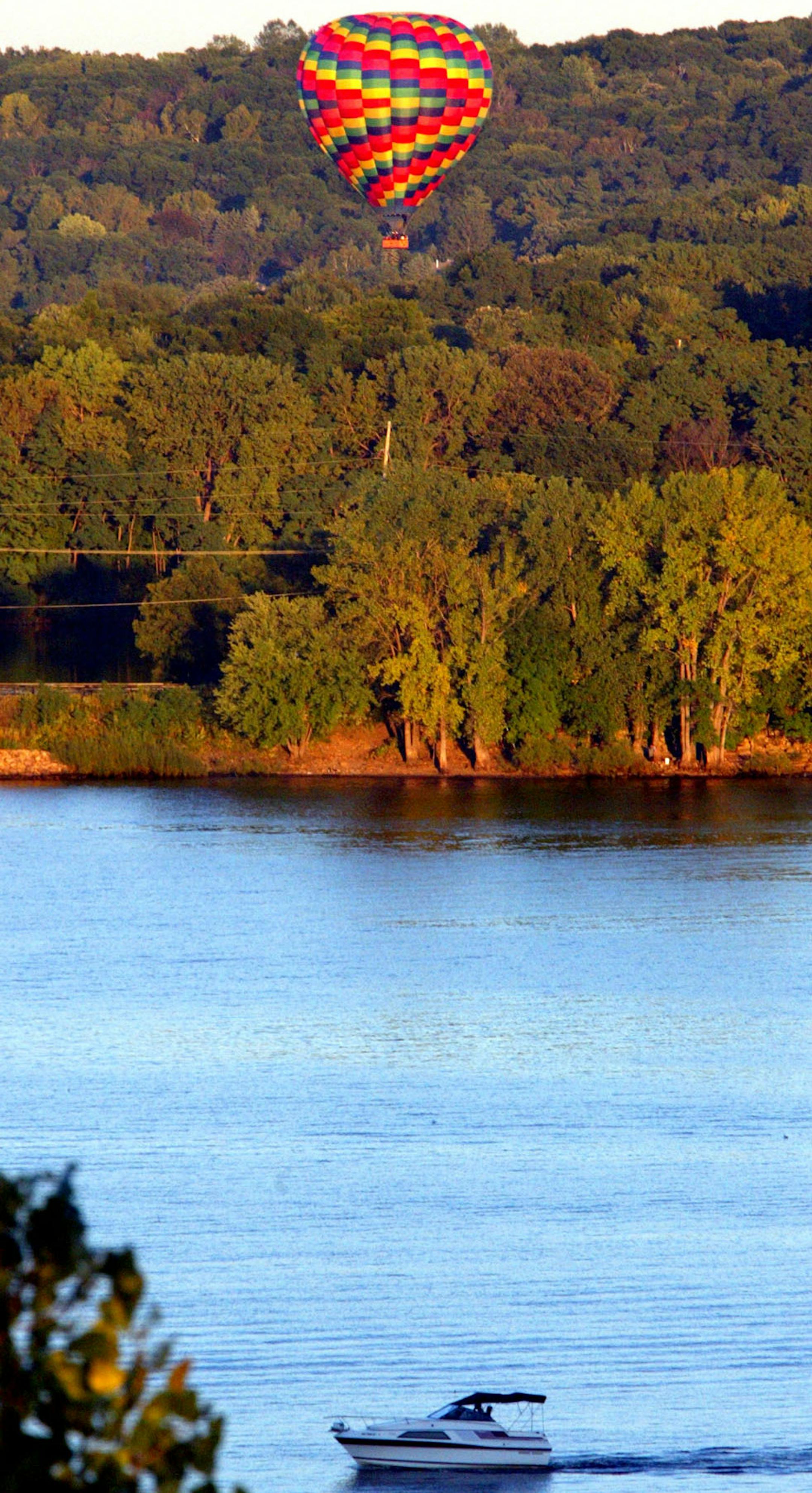Lakeland - 9/15/02 - The Stillwater Balloon Co. gives the public rides in hot air balloons from a landing strip in Lakeland to a landing strip Houlton, Wisc., just across the state line from Stillwater. The hour-long ride follows the path of the St. Croix River, with a capacity of about a dozen people in the gondola. The rides usually occur around dusk when the area winds are most calm.
IN THIS PHOTO: The hot air balloon drifts up the St. Croix River valley as a boater floats along on the river