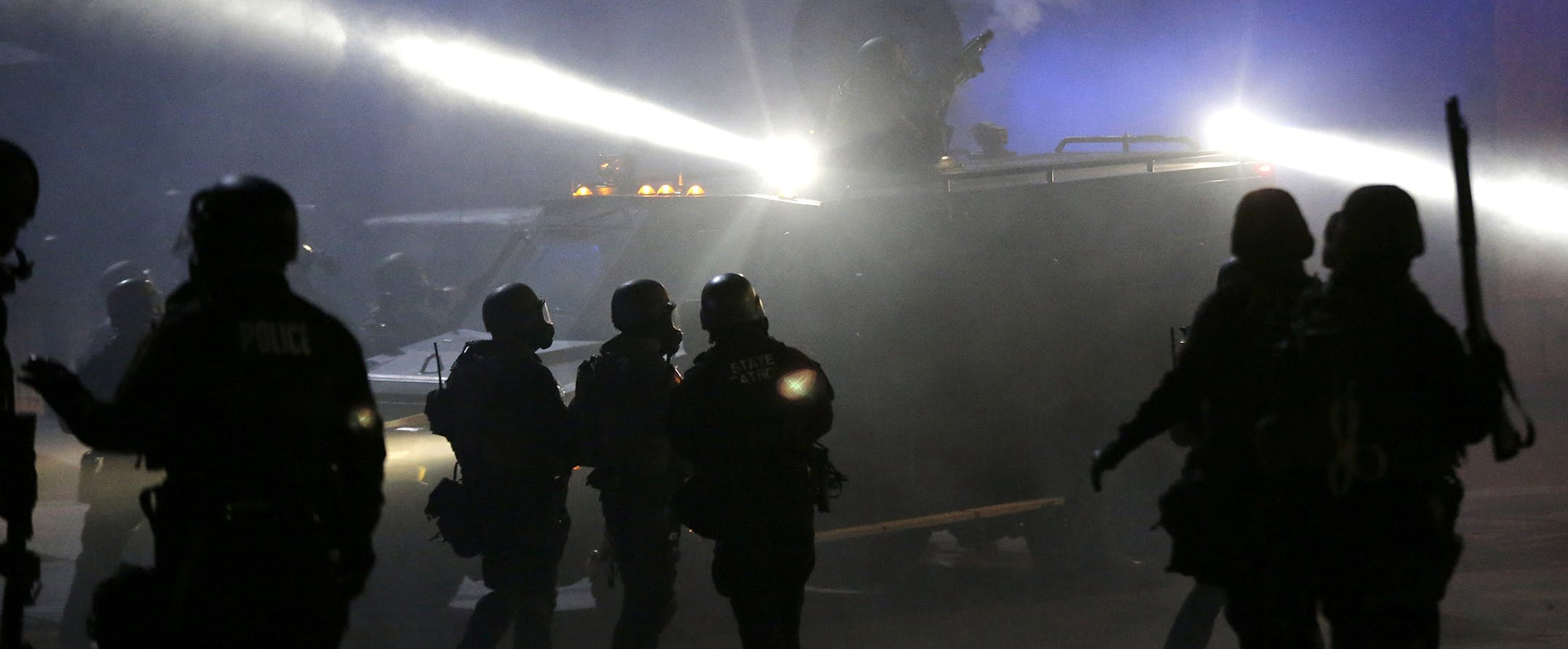 Police in riot gear stand around an armored vehicle as smoke fills the streets Tuesday, Nov. 25, 2014, in Ferguson, Mo. Missouri's governor ordered hundreds more state militia into Ferguson on Tuesday, after a night of protests and rioting over a grand jury's decision not to indict police officer Darren Wilson in the fatal shooting of Michael Brown, a case that has inflamed racial tensions in the U.S. (AP Photo/Charlie Riedel) ORG XMIT: ILKS132