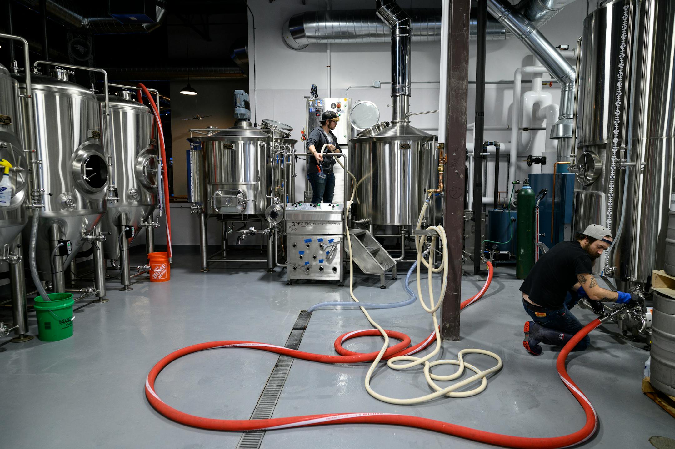 Nine Mile Brewing head brewer John Leingang, right, and assistant brewer Riley Yawn-White work to clean equipment between batches Wednesday, Feb. 9, 2022 at Nine Mile Brewing in Bloomington, Minn.