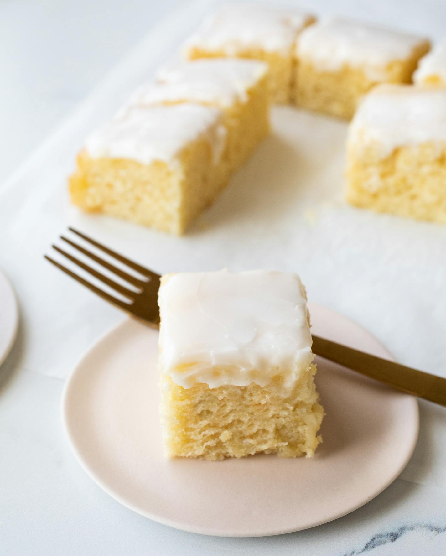 A plate with a slice of lemon snacking cake topped with a lemon glaze.