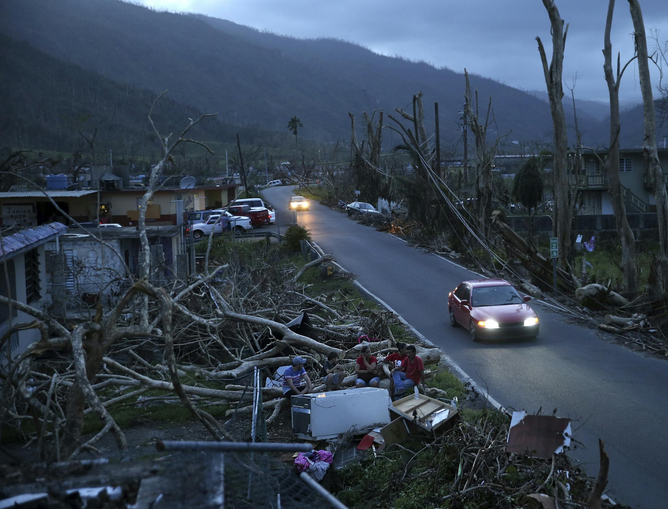 FILE - In this Sept. 26, 2017, file photo, neighbors sit on a couch outside their destroyed homes as sun sets in the aftermath of Hurricane Maria, in Yabucoa, Puerto Rico. U.S. government forecasters are expecting an active Atlantic hurricane season. The National Oceanic and Atmospheric Administration forecast released Thursday, May 24, 2018, calls for about 10 to 16 named storms, with about five to nine hurricanes. (AP Photo/Gerald Herbert, File)