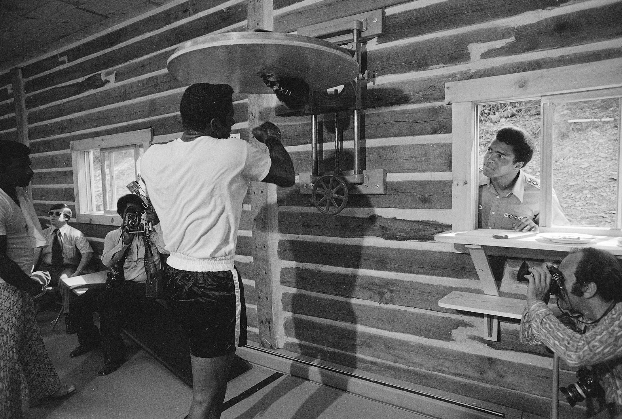 Floyd Patterson works out on a punching bag as Muhammad Ali peeks in the open window of his training camp in Deer Lake, Pa., Sept. 7, 1972. Ali invited Patterson to help him formally dedicate his new training camp and work out for a day. The two heavyweights will face each other in a 12-round bout in New York on Sept. 20.