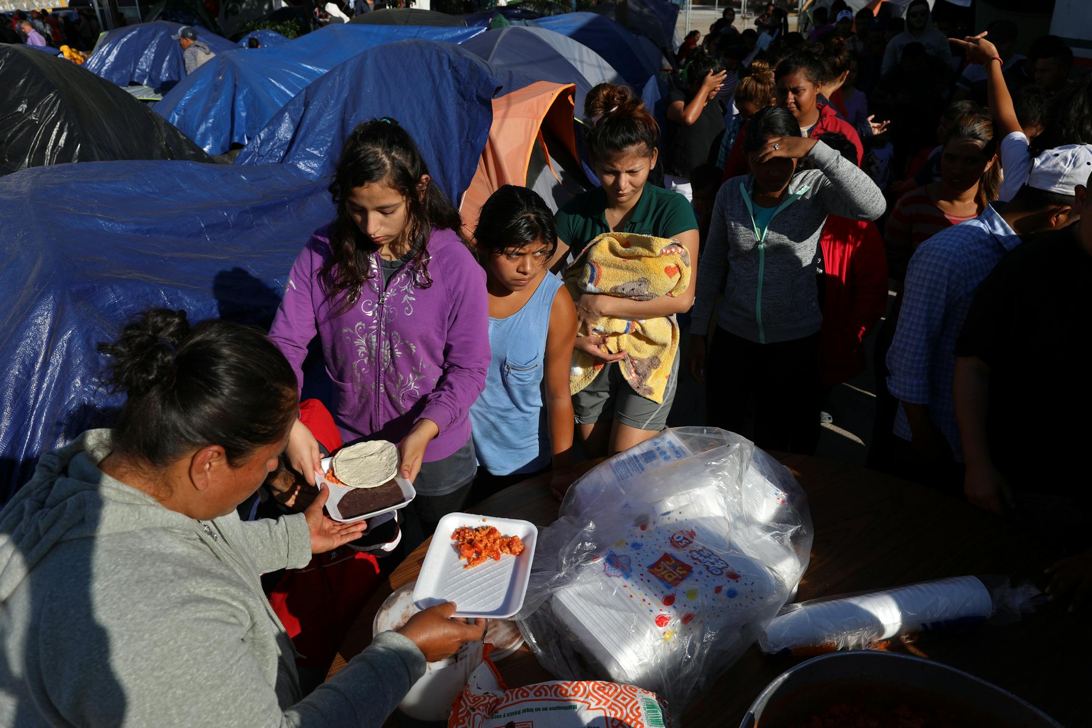Migrants line up as volunteers serve breakfast at an encampment near the banks of the Rio Grande in Matamoros, Mexico. (Gary Coronado/Los Angeles Times/TNS) ORG XMIT: 1512521 ORG XMIT: MIN1912120351566837