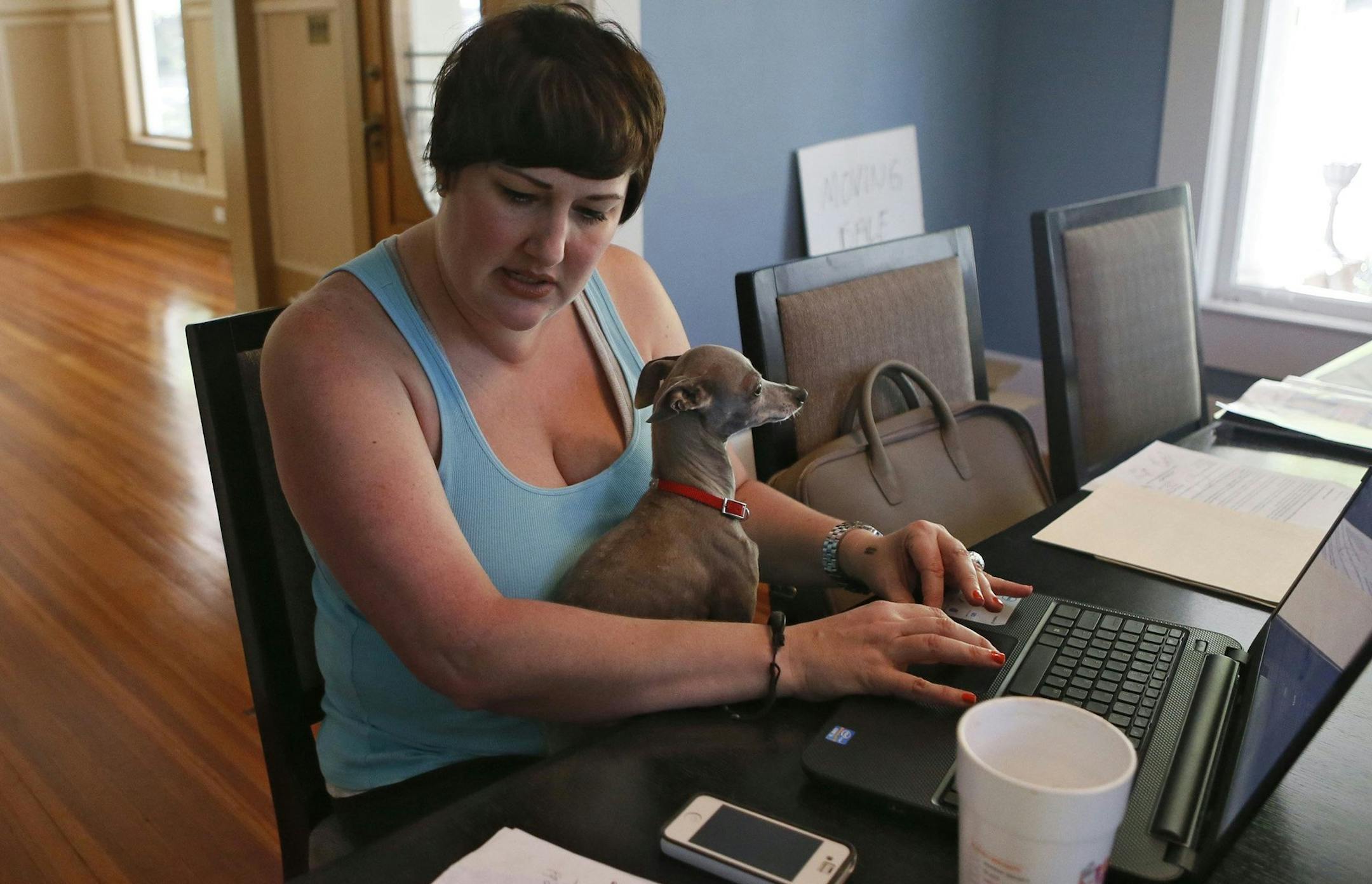 Velvet Bradley works part-time at the dining room table in her home, with her Italian Greyhound, "Sterling," in her lap, while editing a magazine, April 22, 2014, in Rockmart, Ga. The living room behind her is empty because her house has been foreclosed on and she is in the process of moving out. (Bob Andres/Atlanta Journal-Constitution/MCT)