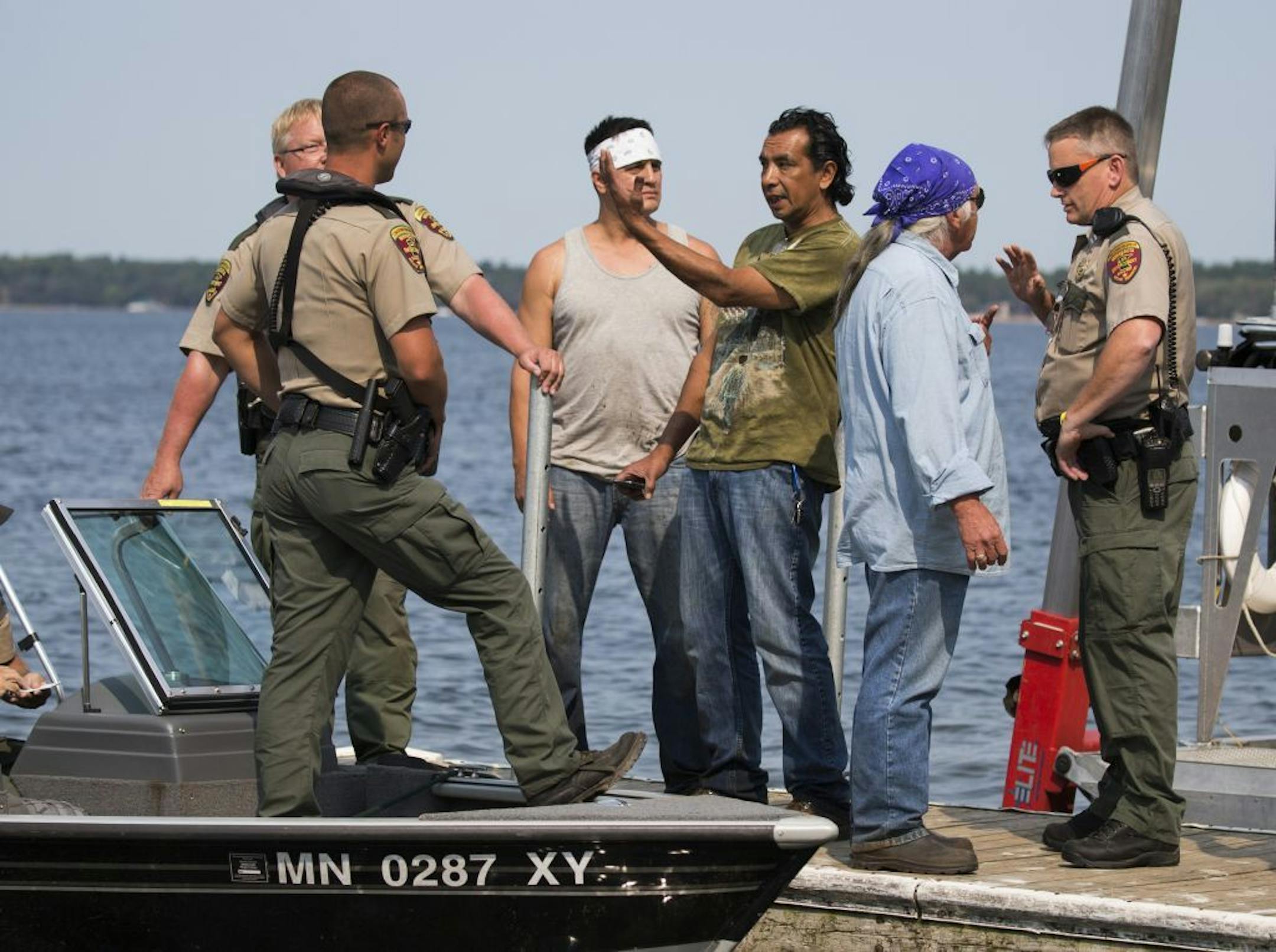 Jim Northrup (center in green shirt) Todd Thompson (left with white headband) and Leonard Thompson (right with blue headband) talk with conservation officers at a public dock after having their nets siezed from Gull Lake.