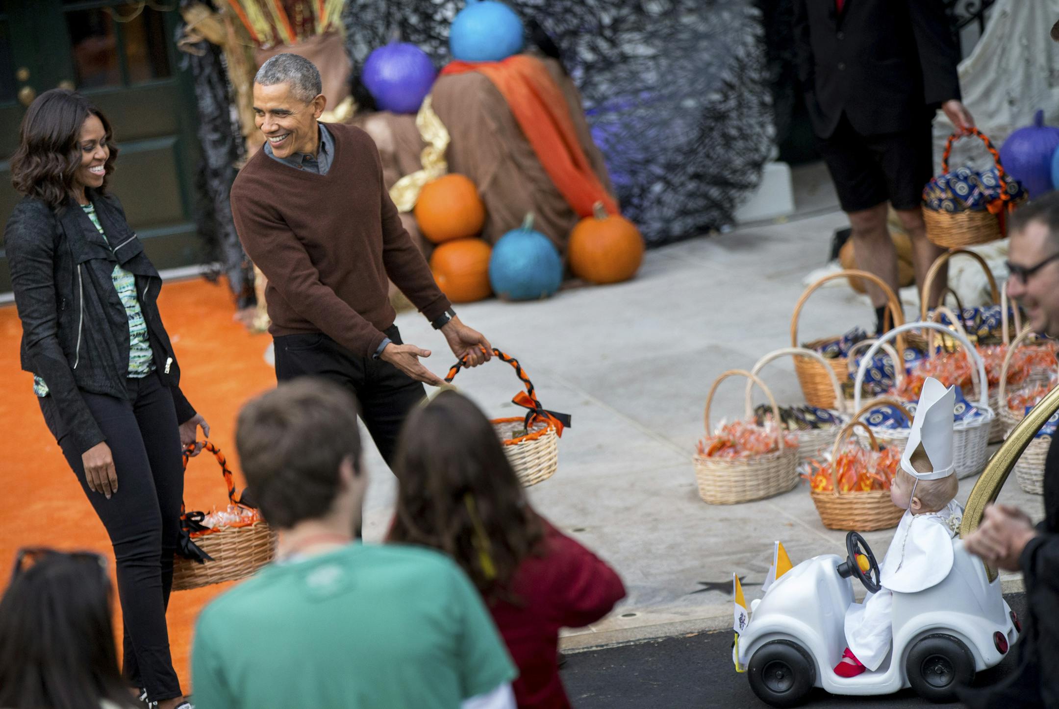 President Barack Obama, accompanied by first lady Michelle Obama, reacts as a child dressed as the Pope approaches in a baby Popemobile during Halloween festivities at the South Portico of the White House in Washington, Friday, Oct. 30, 2015. The first couple welcomed local children and children of military families to 'trick-or-treat' at the White House for Halloween. (AP Photo/Andrew Harnik)