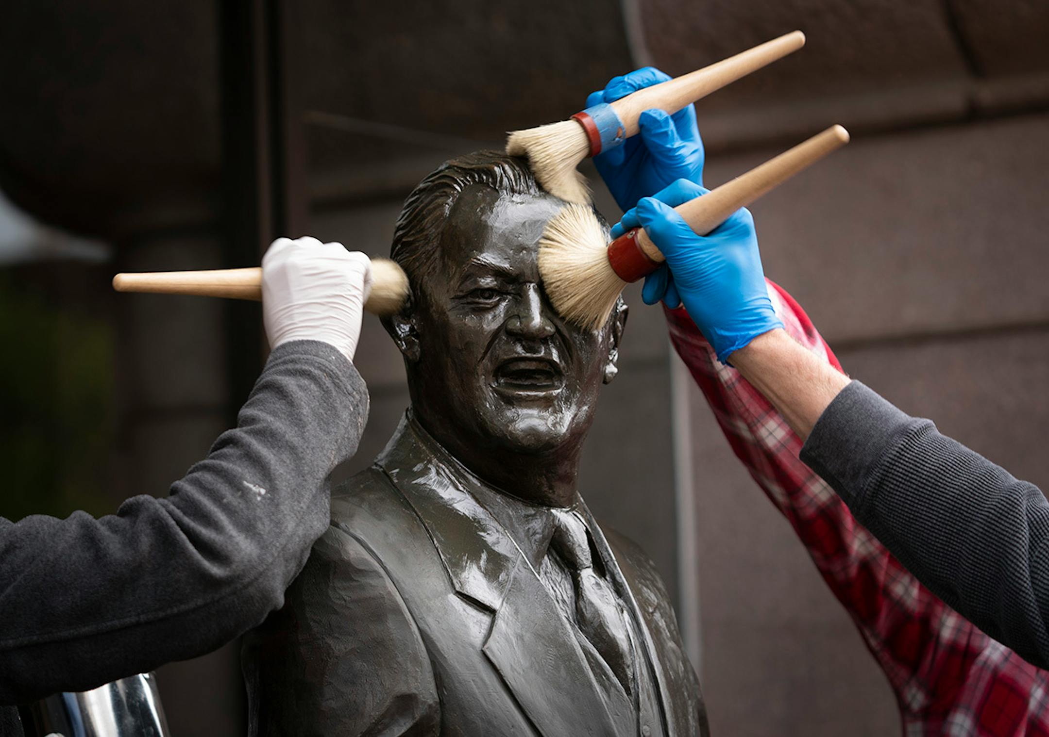 Cassie Rooney, Joel Lundeen and David Fitzgerald used brushes to add wax to the bronze statue of Vice President Hubert Humphrey in front of City Hall on Tuesday, May 28, 2019, in Minneapolis.