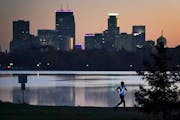 File photo of a runner, wearing an illuminated safety vest, cruising around Bde Maka Ska with the Minneapolis skyline behind at dusk.