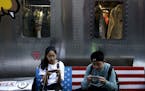 FIEL - In this Sept. 24, 2018, file photo, shoppers sit on a bench with a decorated with U.S. flag browsing their smartphones outside a fashion boutiq