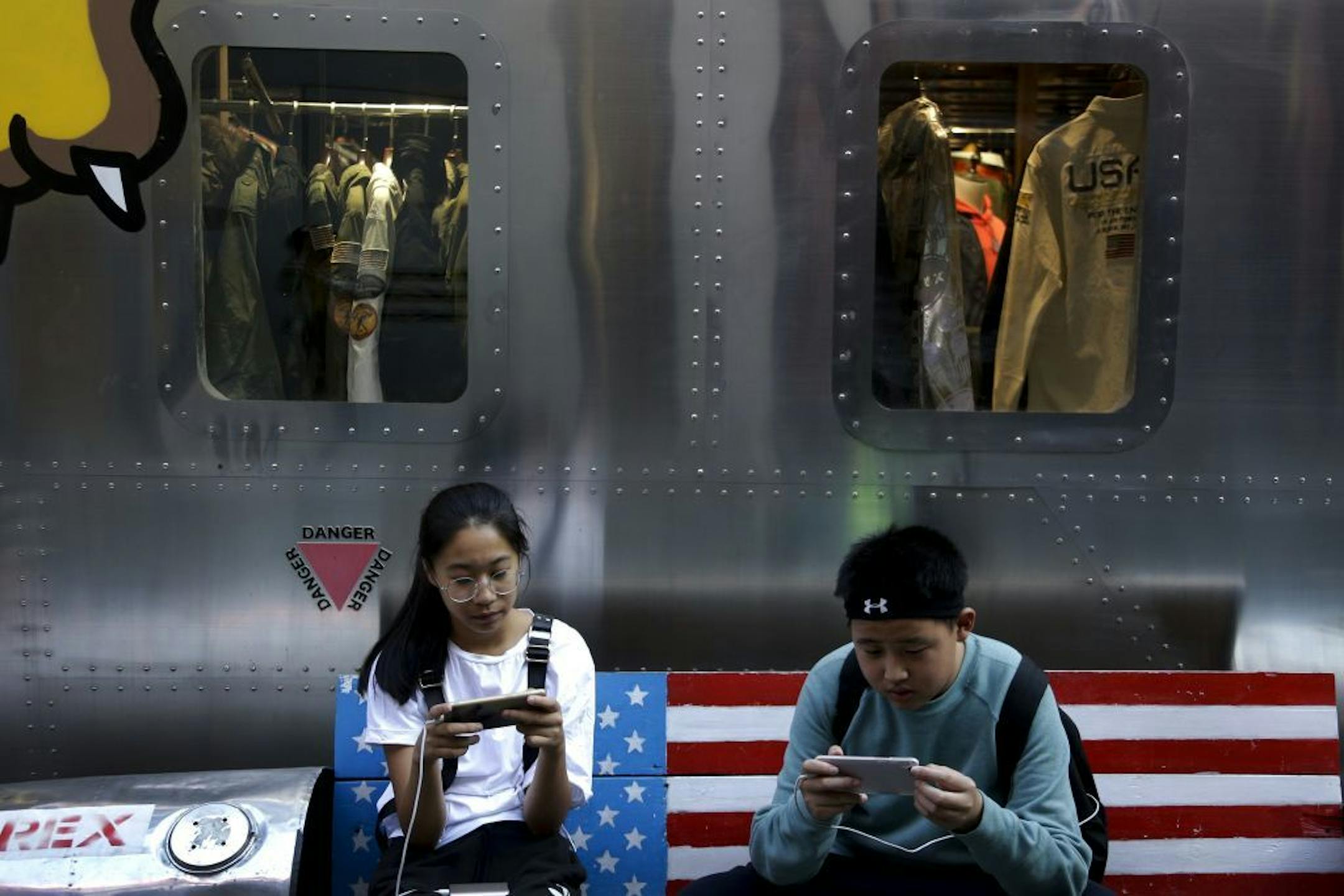 FIEL - In this Sept. 24, 2018, file photo, shoppers sit on a bench with a decorated with U.S. flag browsing their smartphones outside a fashion boutique selling U.S. brand clothing at the capital city's popular shopping mall in Beijing. China will go along with changes meant to update global trade rules but they must protect Beijing's status as a developing country, a Cabinet official said Friday, Nov. 23, 2018.