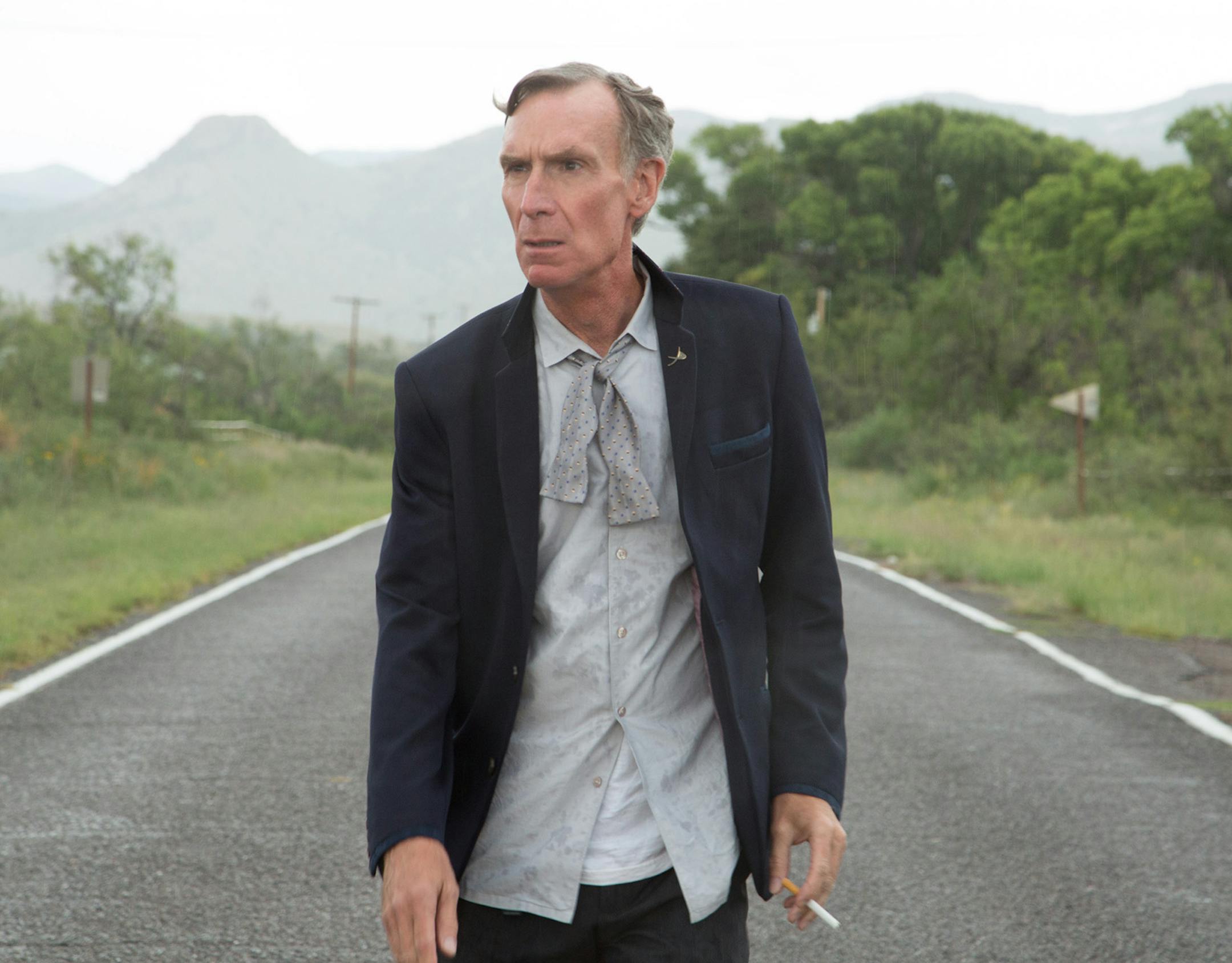 CLIFF, N.M.- After hearing depressing news about the state of the planet, Bill Nye walks in despair smoking a cigarette in the middle of the road. (Photo Credit: NG Studios/Chris Cassel) ORG XMIT: NG Studios