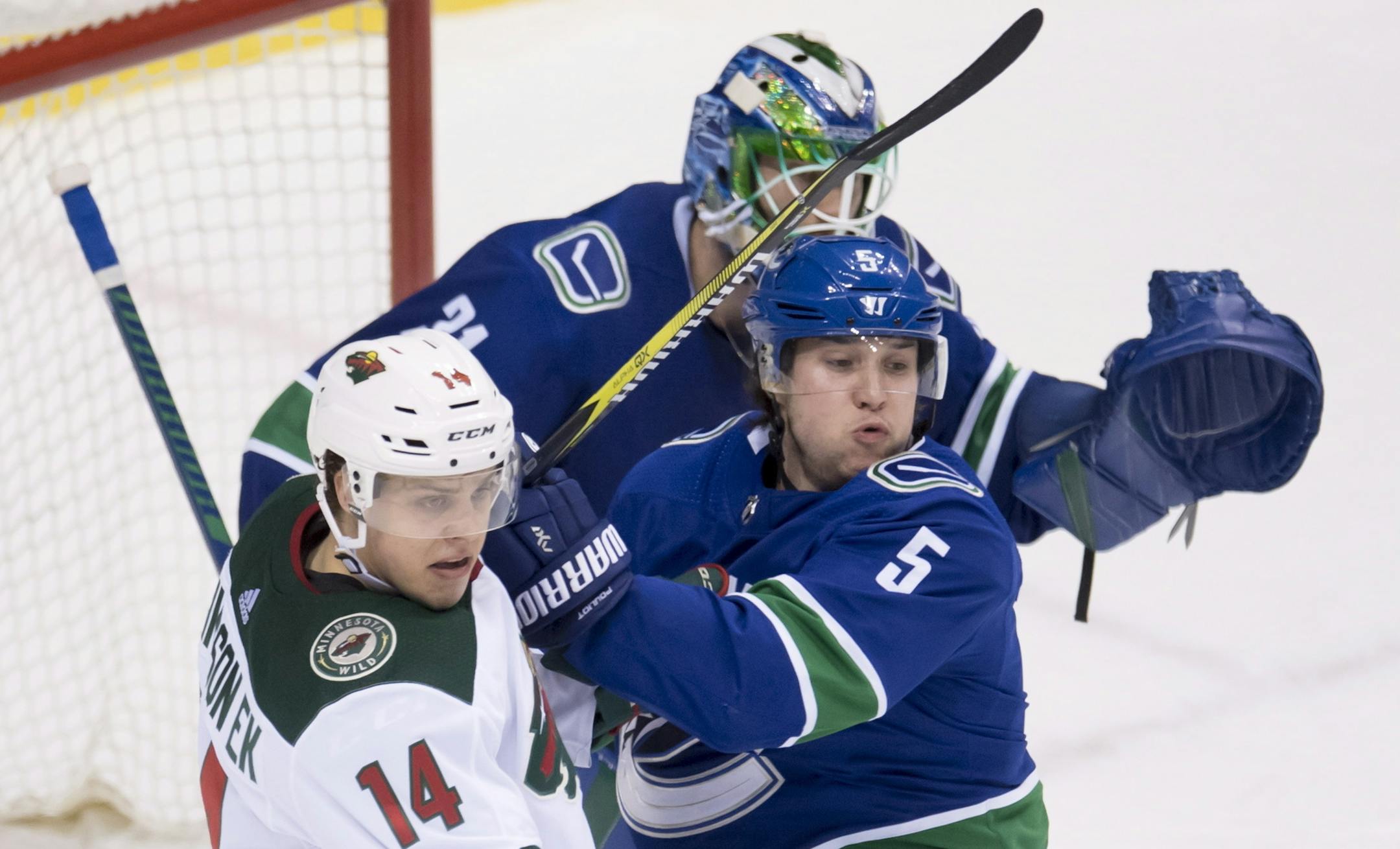 Vancouver Canucks defenseman Derrick Pouliot (5) tries to clear Minnesota Wild centre Joel Eriksson Ek (14) from in front of Canucks goaltender Anders Nilsson (31) during the second period of an NHL hockey game Friday, March 9, 2018, in Vancouver, British Columbia. (Jonathan Hayward/The Canadian Press via AP)