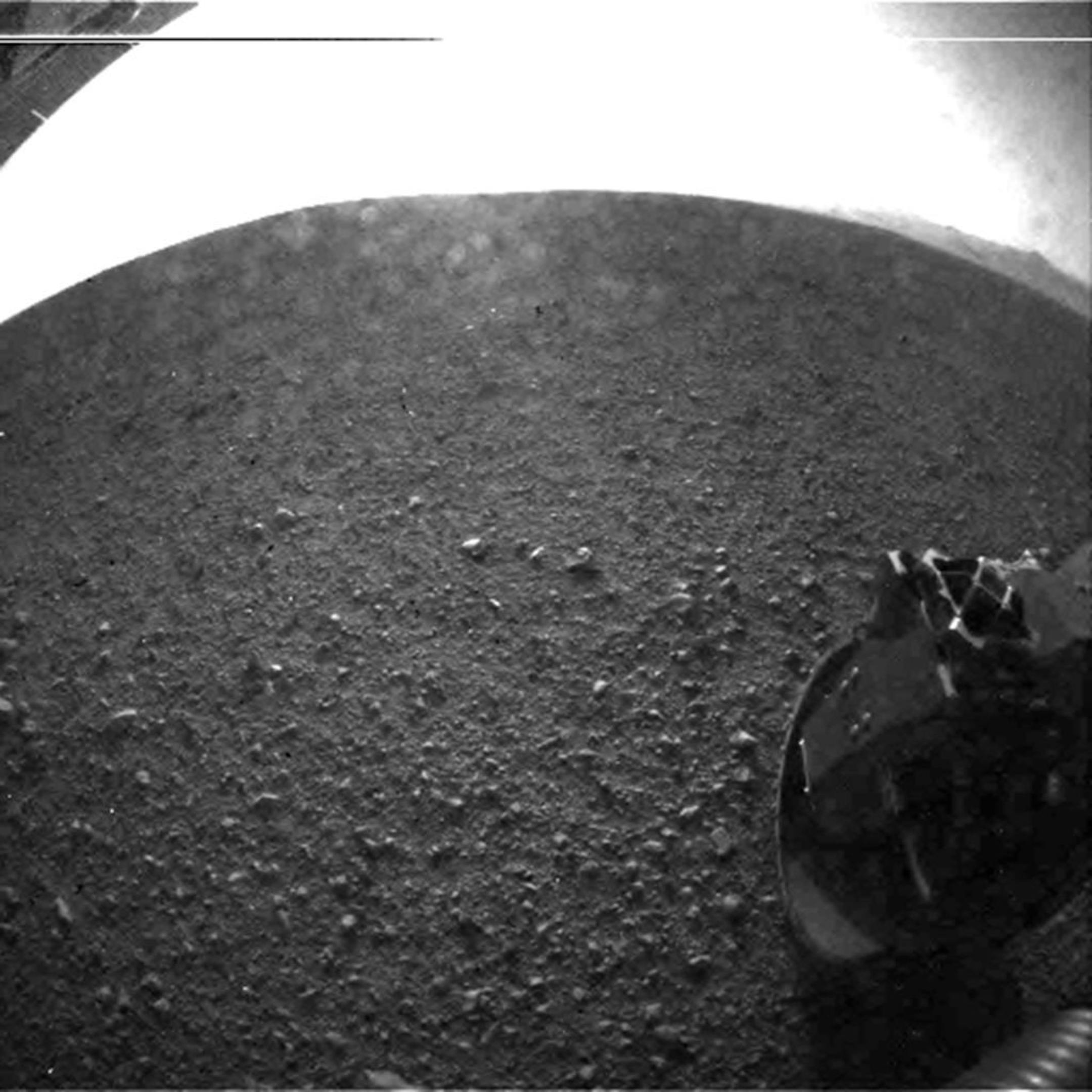 This photo provided by NASA's Jet Propulsion Laboratory shows the gravel on the surface of Mars' Gale Crater where the Curiosity rover landed late Sunday, Aug. 5, 2012 PDT. On the horizon is the rim of the crater. Part of the spring that released the lens' dust cover can be seen at the bottom right, near the rover's wheel. At top left is part of the rover's power supply. The lines across the top are an artifact from the sensor since the camera is looking into the sun.