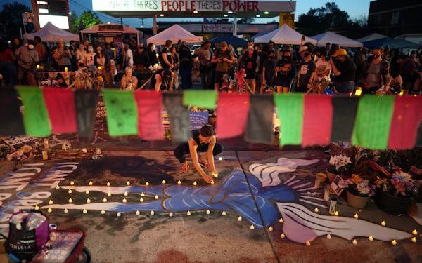 Ali Tennant places candles around an angel painted on the sidewalk at George Floyd Square during a day long celebration on Tuesday, May 25, 2021 to co