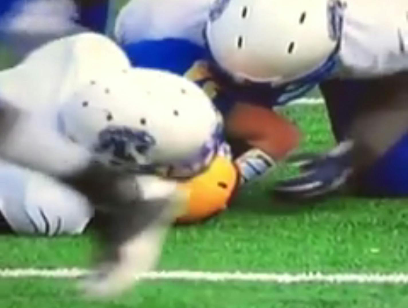 In this screenshot of a slow motion replay, a player from Minneapolis North appears to reach into the helmet of a rival player after a tackle.