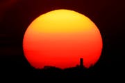 The sun sets behind a smokestack in the distance in Kansas City, Mo.