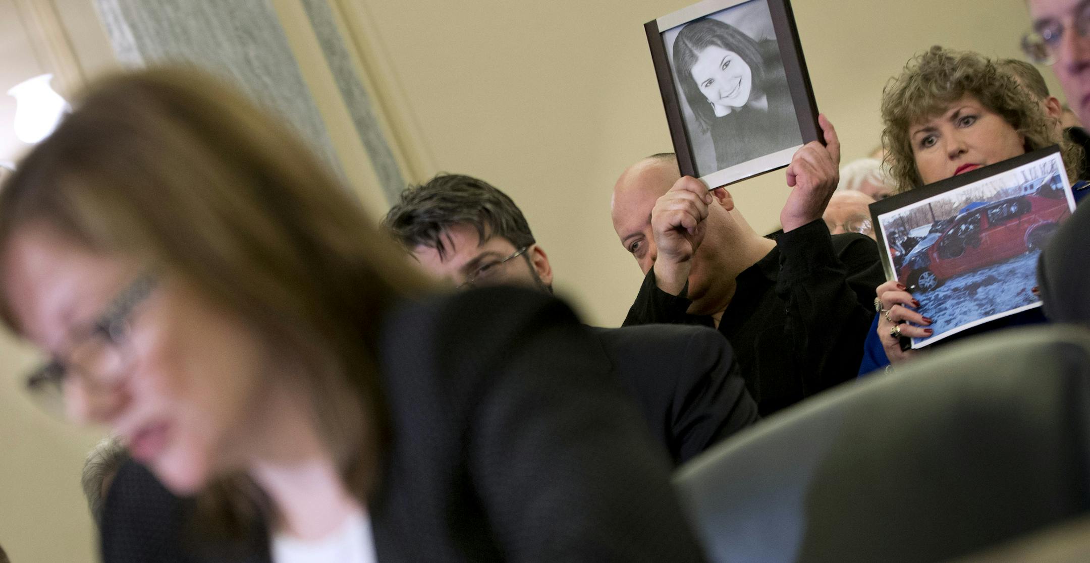 Leo Ruddy, center, and his wife Mary Theresa Ruddy, right, from Scranton, Pa., holds up photographs of their daughter Kelly Erin Ruddy and the 2005 Chevy Cobalt that she crashed and died, as they sit in the audience to listen to testimony by General Motors CEO Mary Barra, left, on Capitol Hill in Washington, Wednesday, April 2, 2014, before the Senate Commerce, Science and Transportation subcommittee. The subcommittee is looking for answers from Barra about safety defects and mishandled recall o