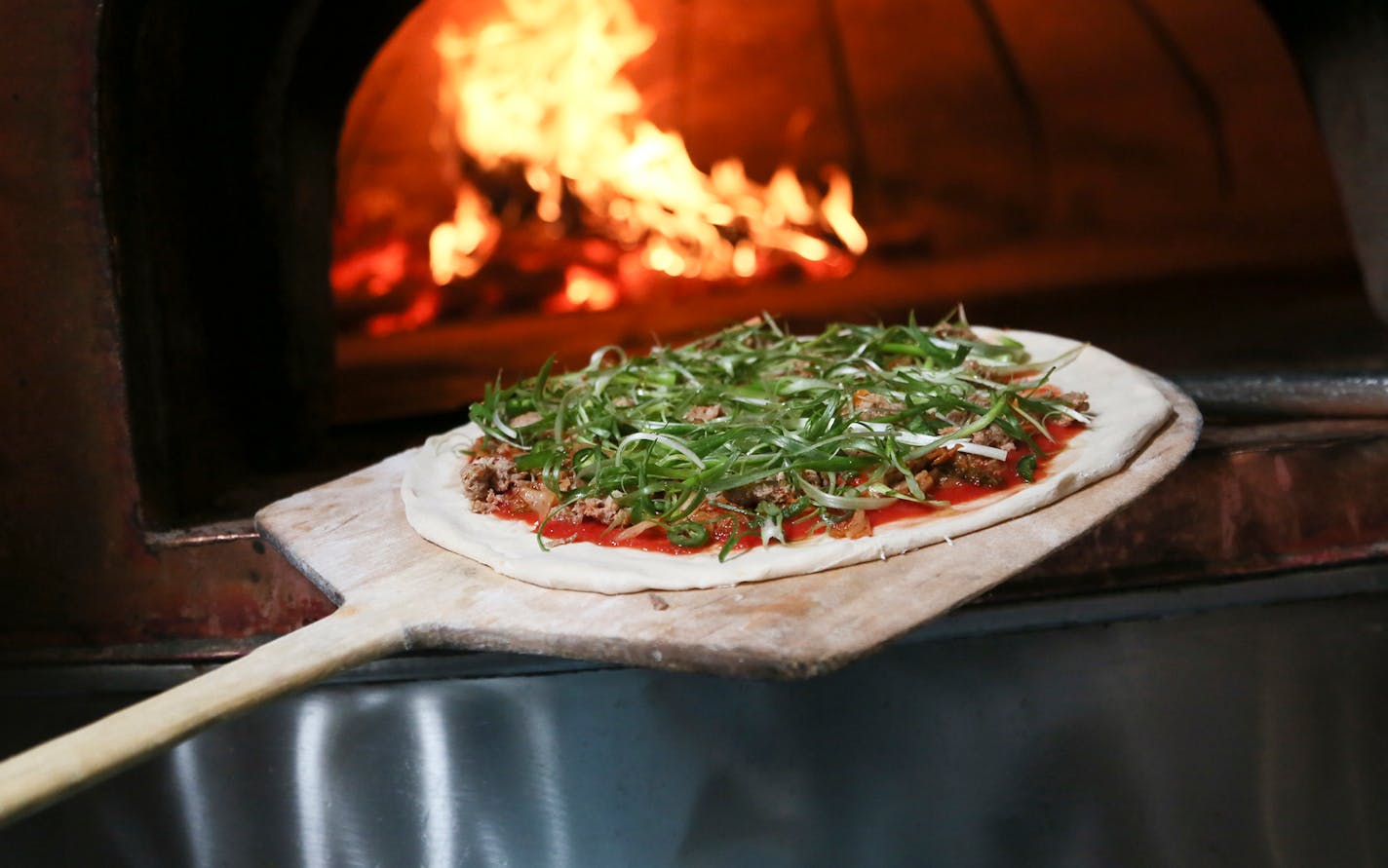 At Pizzeria Lola, pizza chef Bishara Sahoury places the Lady Za Za pizza in the LePanyol pizza oven fired with seasoned red oak at temps of 650 degrees or higher. The kim chi based pizza is made with Italian red sauce, house-made kimchi, Korean sausage, serrano peppers, scallions and sesame and soy chilli glaze Friday, April 11, 2014, in Minneapolis, MN.](DAVID JOLES/STARTRIBUNE) djoles@startribune.com Story on the popularity of a Korean cabbage food - from gourmet pizza to a general mills product - owner Ann Kim offers a pizza made with it.**Bishara Sahoury,cq