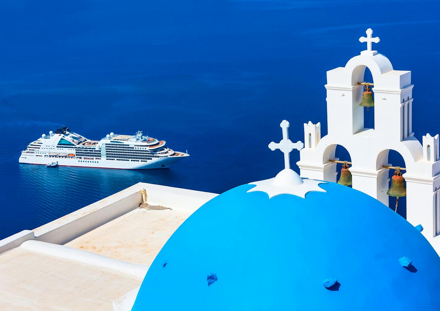 Oia, Santorini, Greece - April 25, 2019: Iconic view of blue and white church dome and bell tower, sea and cruise ship