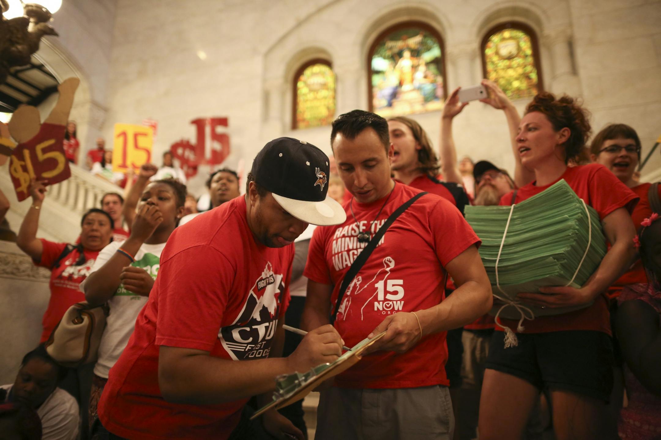 While Steven Suffridge signed the petition to be the 20,001st supporter, Ginger Jentzen held the stack of signed petitions in support of a $15 minimum wage as demonstrators rallied in City Hall and heard speeches before handing over a petition with 20,000 signatures on it to the City Clerk.