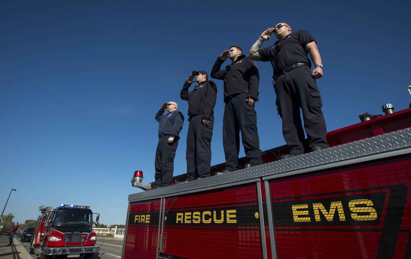 Brooklyn Park firefighters, from left, Dave Schmidt, Brandon Hollingsworth, Taylor Anderson and Pat Roepke stood atop a fire truck on the Interstate 94 overpass on Zane Avenue N. to salute the parade of police vehicles escorting the fallen deputy's body.