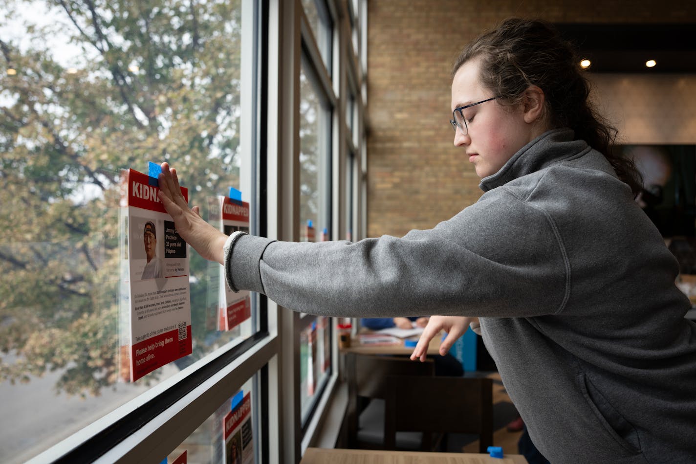 Senior Isabel Lundquist tapes double-sided kidnapped flyers on the windows at the University of Minnesota Hillel in Minneapolis, Minn., on Friday, Nov. 3, 2023.