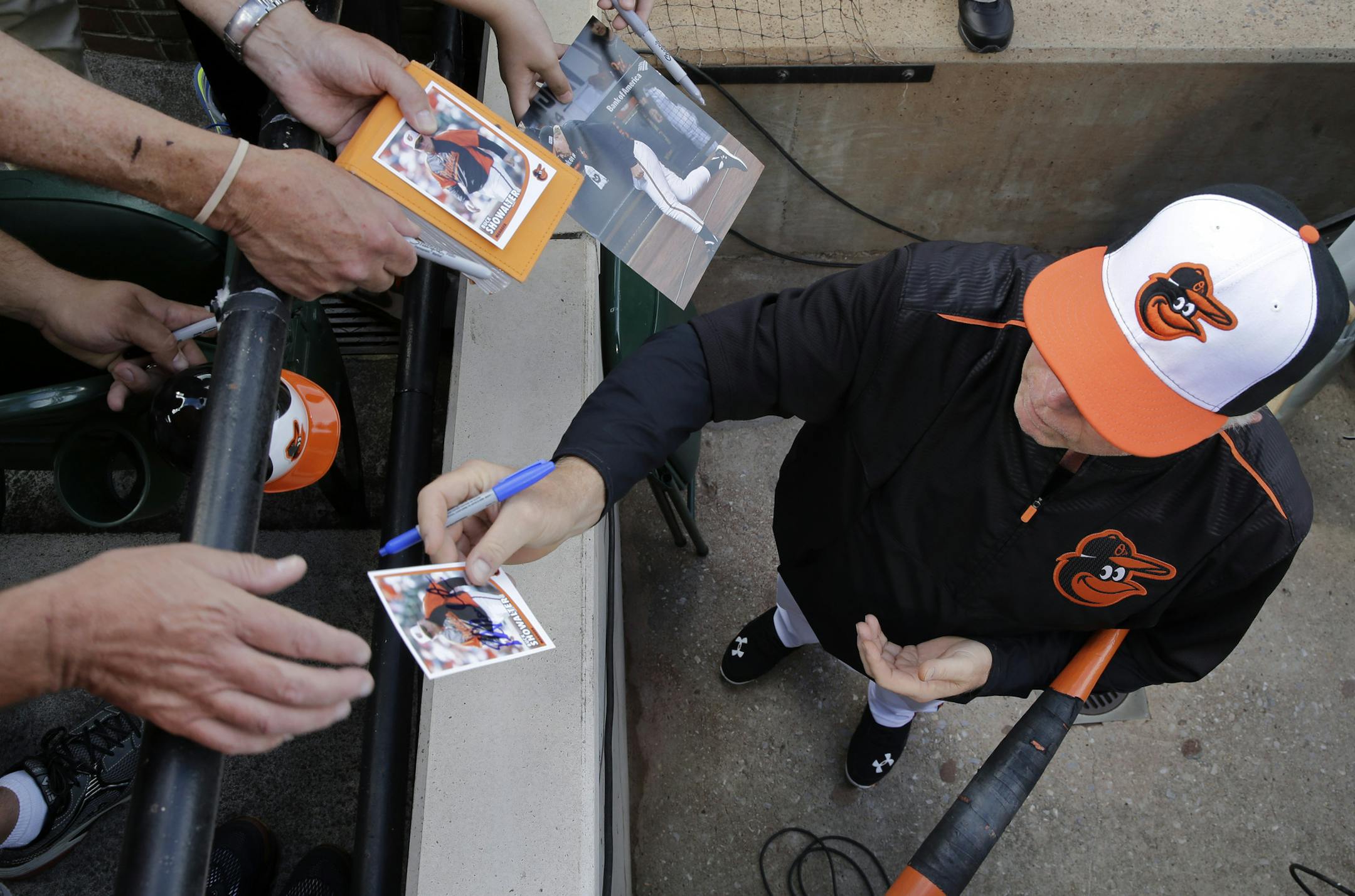 Baltimore Orioles manager Buck Showalter, right, signs autographs for fans before a baseball game against the Toronto Blue Jays, Monday, May 11, 2015, in Baltimore. Playing in front of their home fans for the first time in two weeks, the struggling Orioles hope a game at Camden Yards can serve as a pick-me-up for themselves and the beleaguered city. (AP Photo/Patrick Semansky)