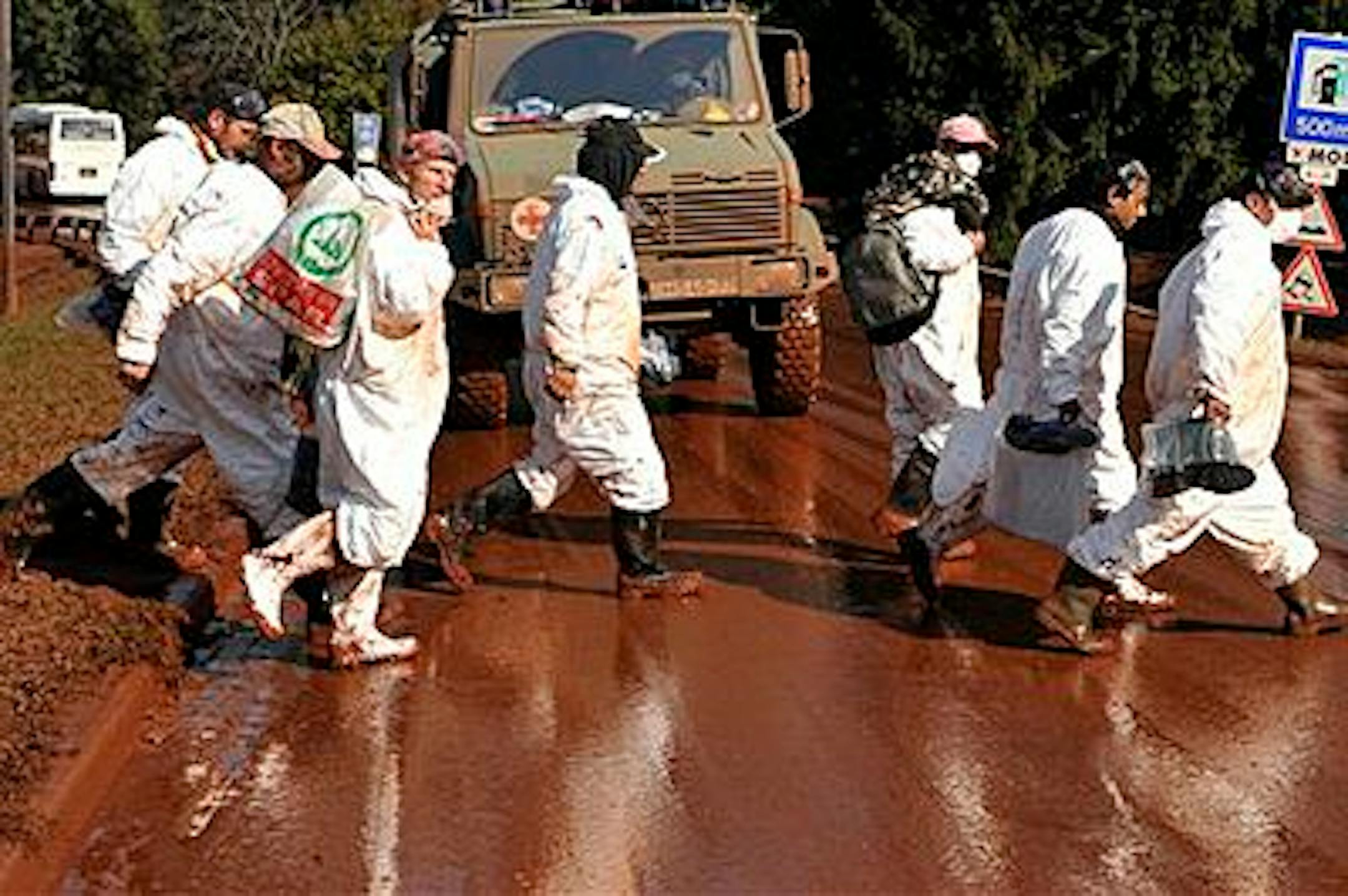 Volunteers, wearing protective gears, walk across a street covered by toxic red sludge in Devecser, Hungary, Monday, Oct. 11, 2010. The population of the neighboring town of Kolontar was evacuated Saturday and Devecser with a population of 5,300 is also in the likely path of a possible new sludge deluge. (AP Photo/Bela Szandelszky)