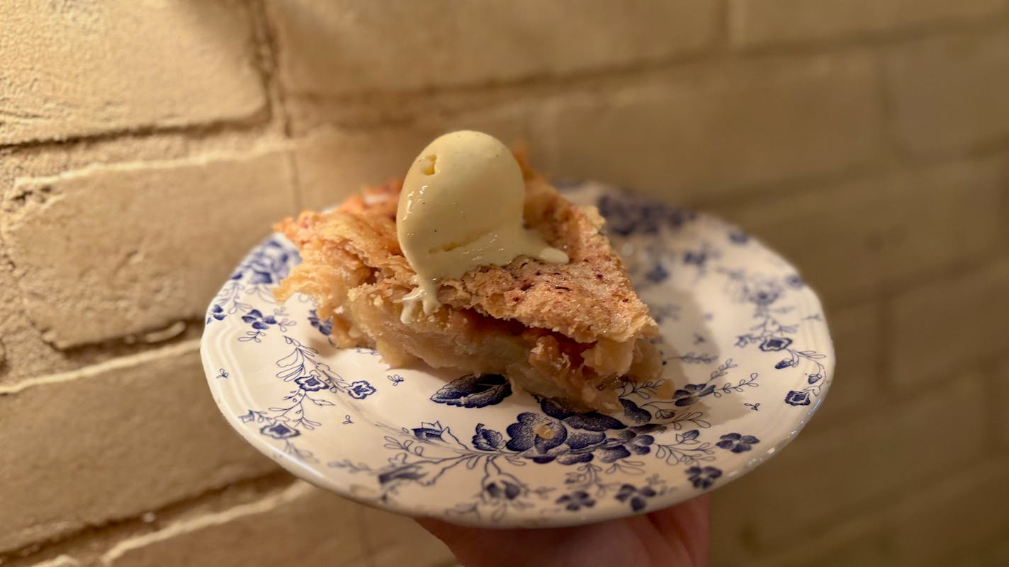 A blue and white china plate holds a slice of apple pie with a scoop of vanilla ice cream on top.