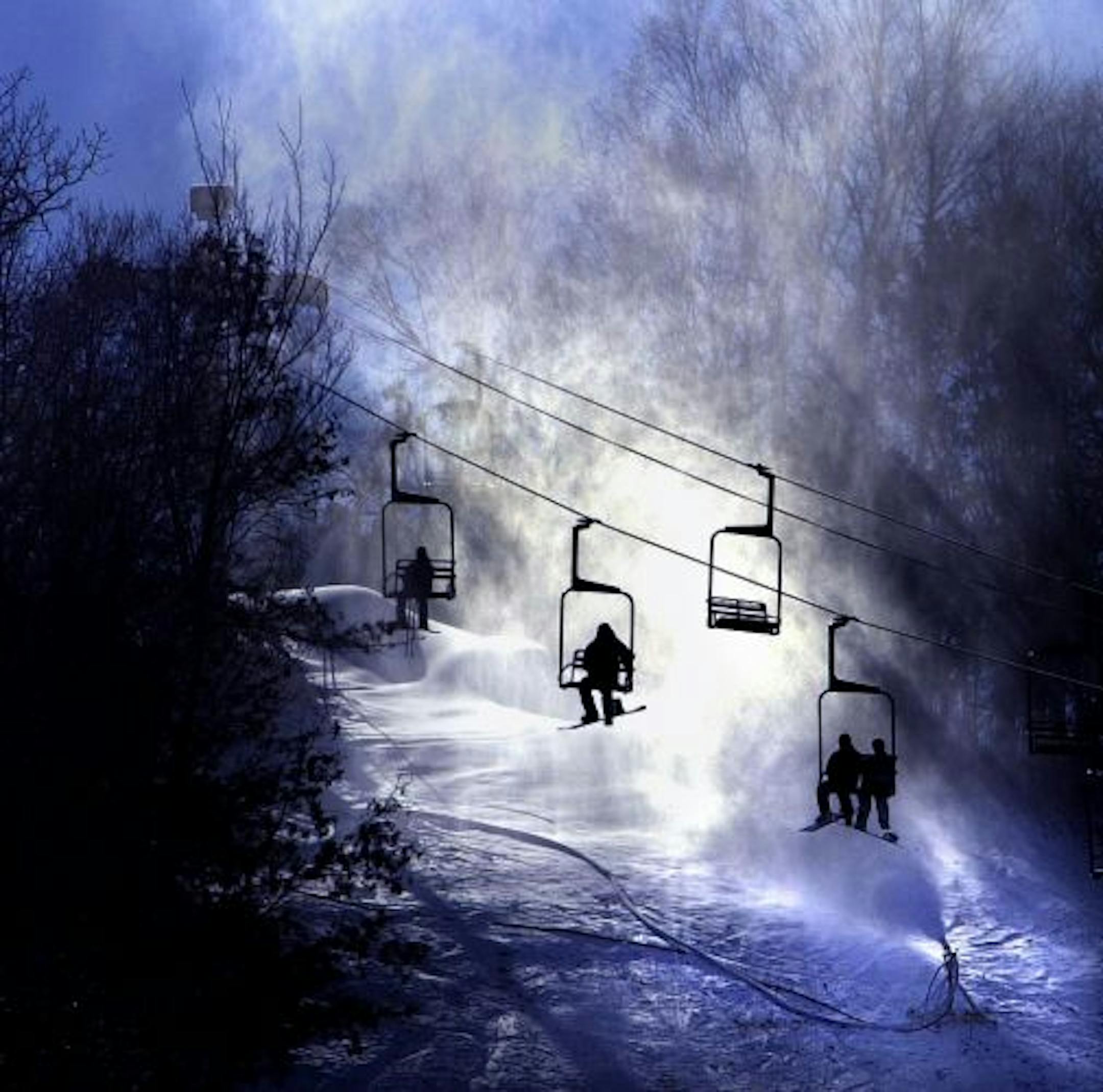 Skiers on chair lift pass by a snowmaking gun enroot to the top of Afton Alps Ski Area.