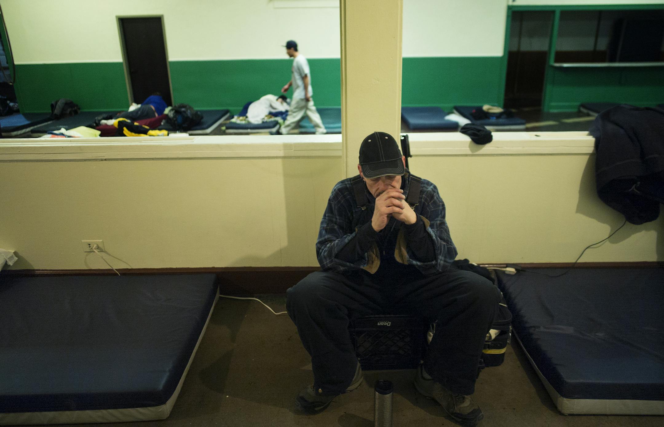 At the shelter housed in the basement of Simpson United Methodist Church, David Thompson listened to some music next to the mattress where he would sleep on a night where the wind chill was expected to dip to 20 below zero.] The Minneapolis City Council is considering a proposal to remove a requirement that homeless shelters be run by religious organizations. The current system means shelter locations are limited to religious facilities and are not always convenient for clients. But residents wo