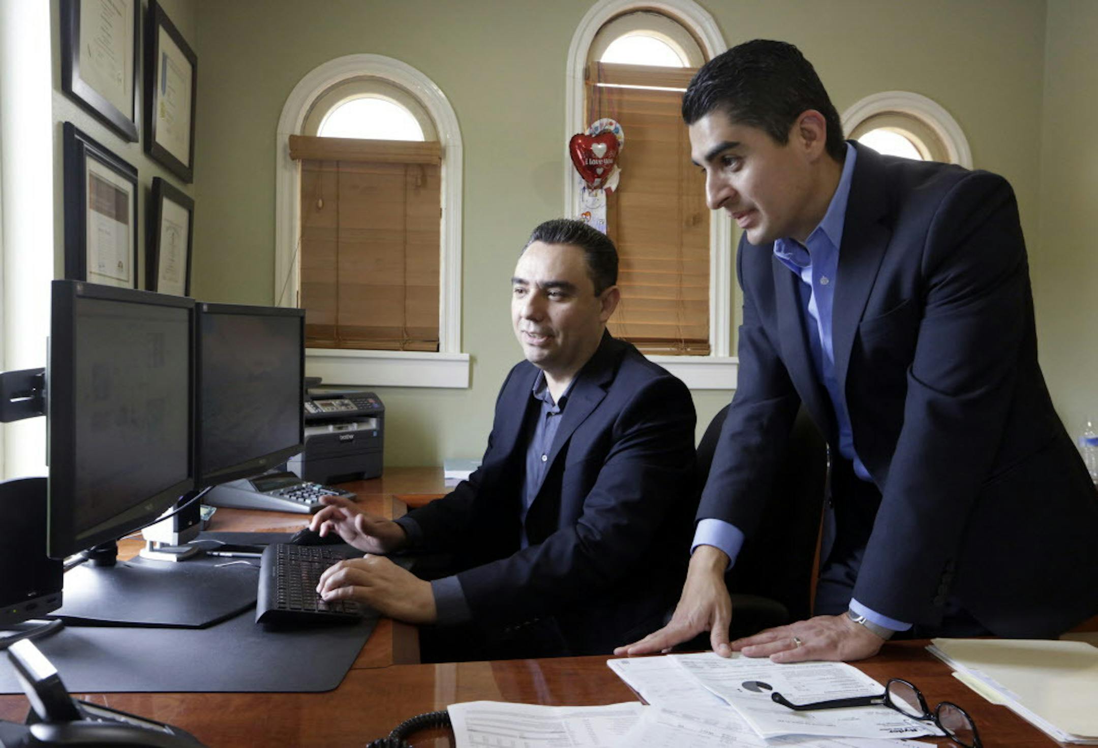In this Friday, Aug. 21, 2015 photo, certified financial planners Aaron Munoz, left, and Gilbert Cerda, pose for a photo at their offices in Downey, Calif. Their company, Cerda Munoz Advisors, offers financial advice with a focus on the Hispanic population. (AP Photo/Damian Dovarganes)