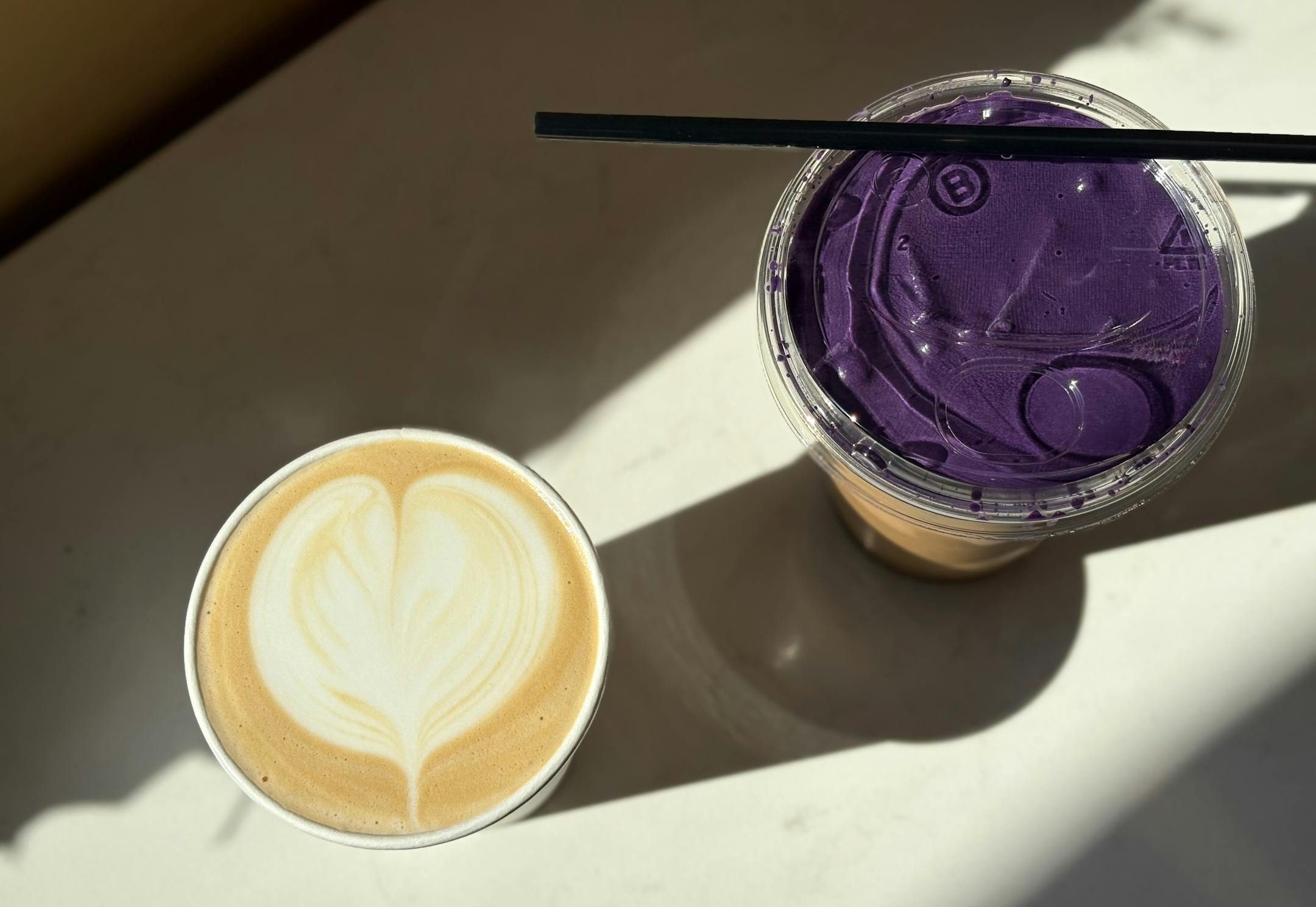 Two lattes, one hot with a heart in the milk foam and another iced and topped with vibrant, purple ube.