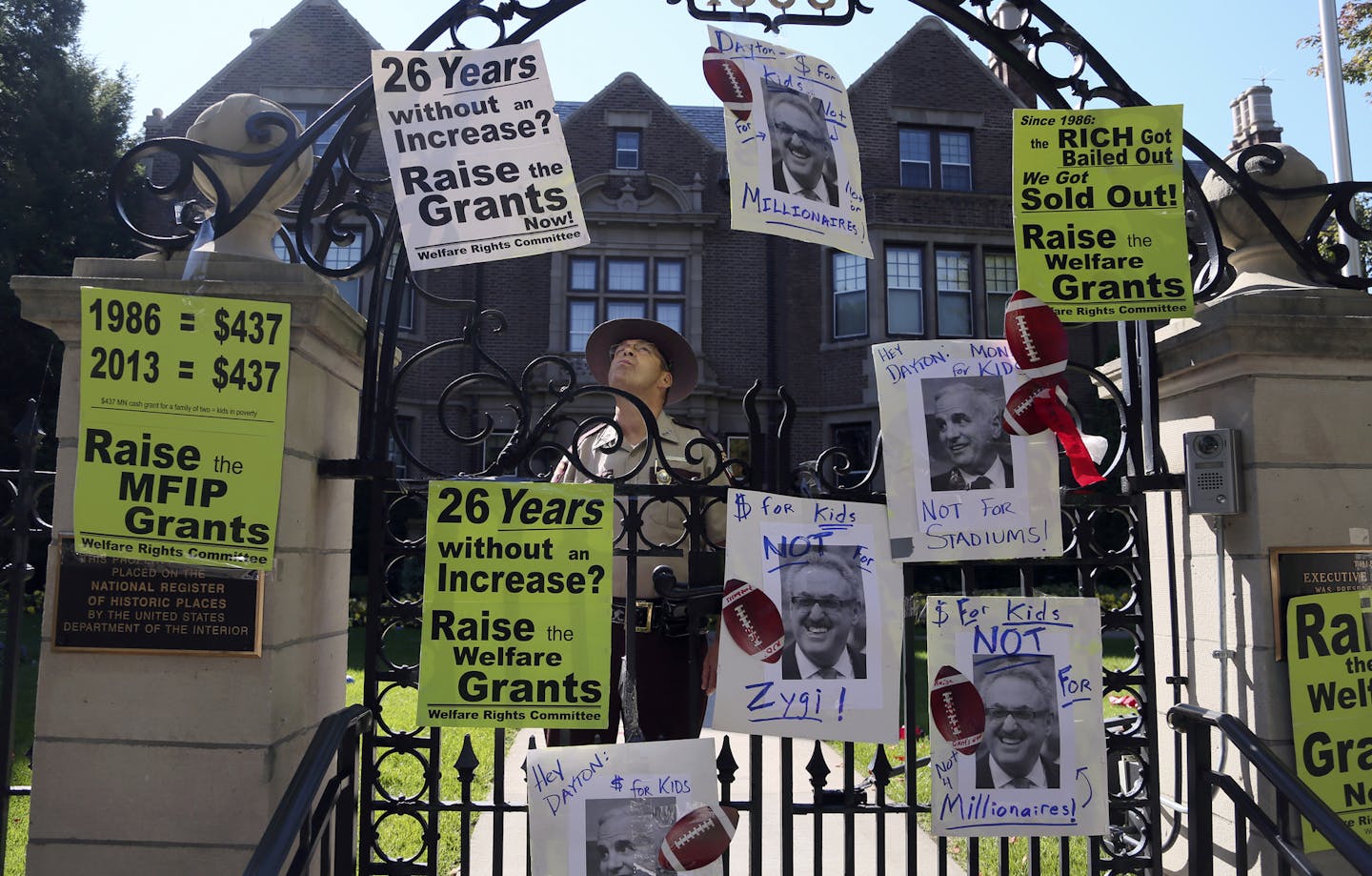 Minnesota State Patrol officer Brent Messer eyes up posters taped to the gate following the Welfare Rights Committee rally Wednesday, Sept. 25, 2013, outside the Governor's Residence in St. Paul, MN.](DAVID JOLES/STARTRIBUNE) djoles@startribune.com Members of the Welfare Rights Committee will rally in front of the Governor's Residence and send messages of "Help poor kids, not millionaires" to the governor attached to footballs.**Brent Messer,cq