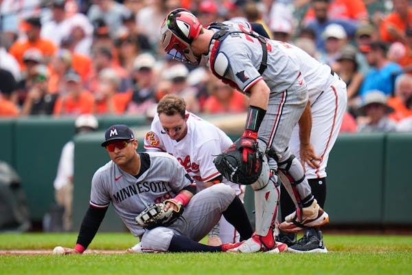 Minnesota Twins first baseman Donovan Solano, left, and Baltimore Orioles' Austin Hays, center, are on the ground after a collision on a groundout by 