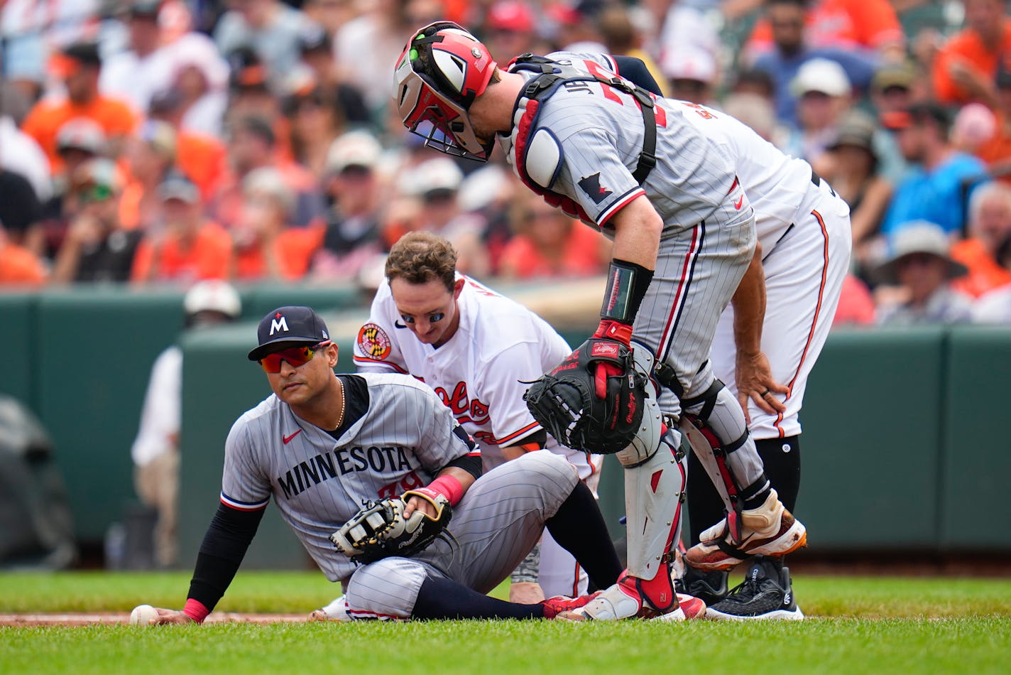 Minnesota Twins first baseman Donovan Solano, left, and Baltimore Orioles' Austin Hays, center, are on the ground after a collision on a groundout by Hays in the second inning of a baseball game, Sunday, July 2, 2023, in Baltimore. Twins catcher Ryan Jeffers, right, and Orioles' first base coach Anthony Sanders, back right, check in on them. (AP Photo/Julio Cortez)