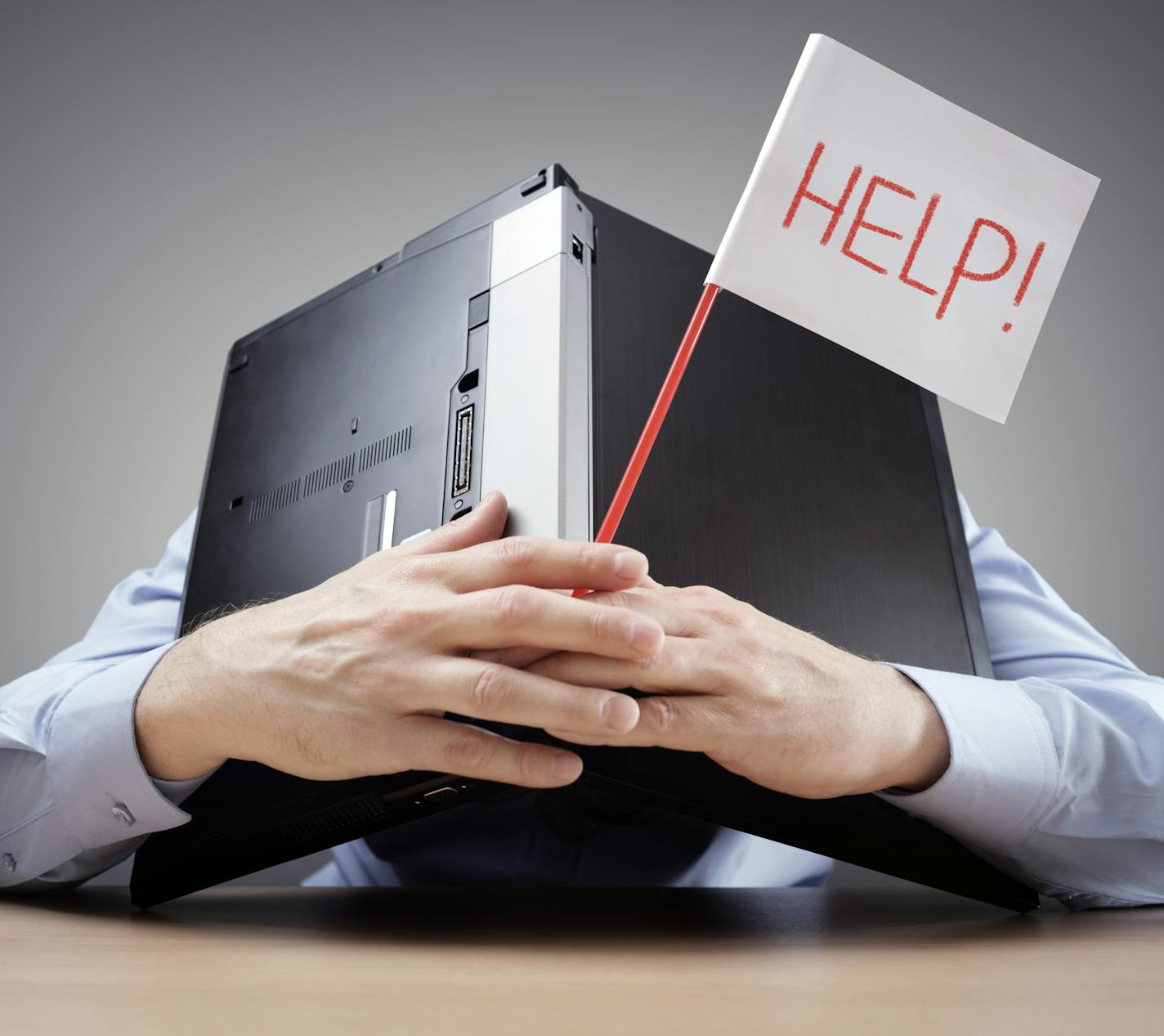 Frustrated and overworked businessman burying his head uner a laptop computer asking for help