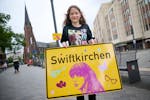 Schoolgirl Aleshanee Westhoff shows a "Swiftkirchen" town sign in honor of musician Taylor Swift in Gelsenkirchen, Germany, Tuesday, July 2, 2024.