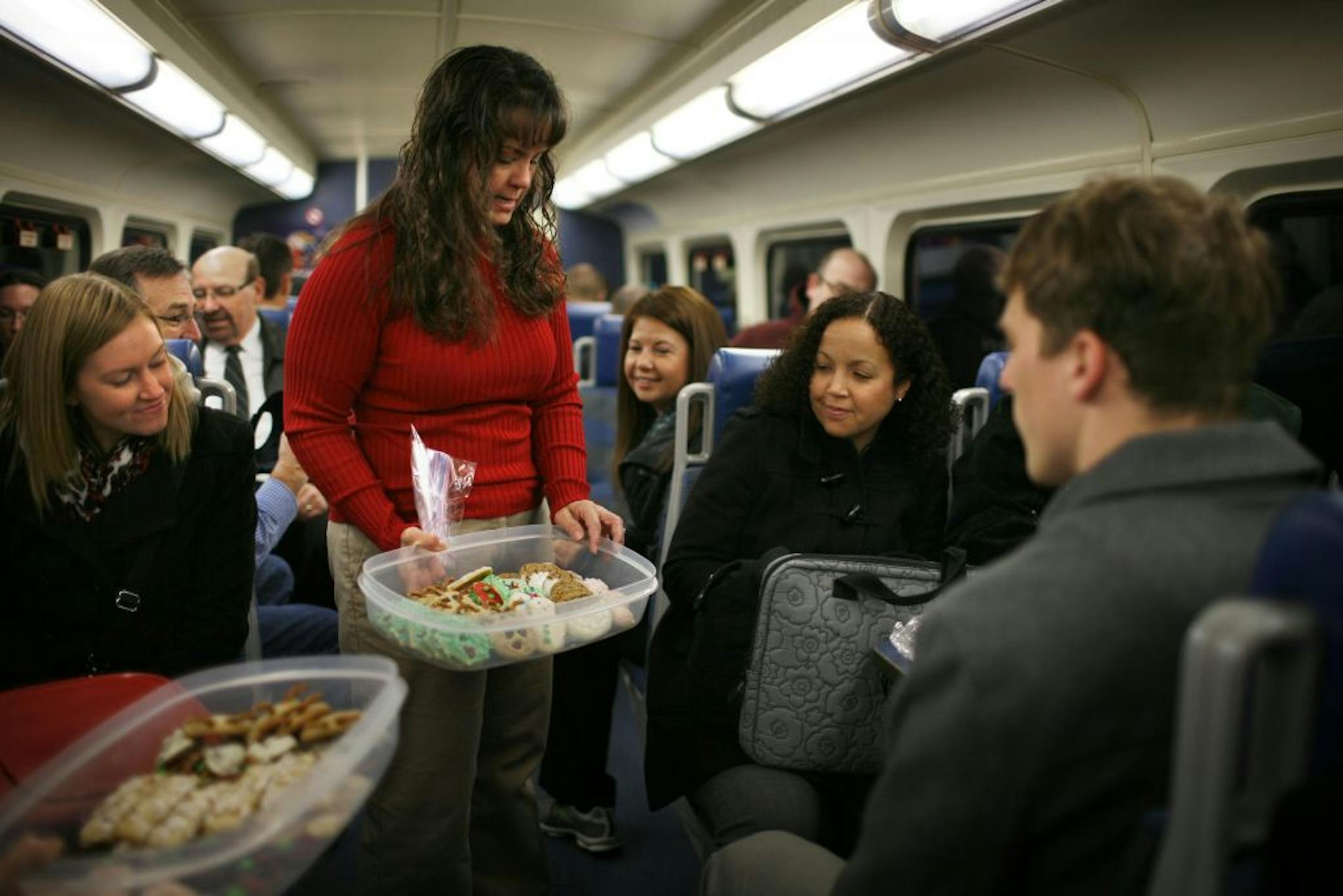 Northstar rider Jill Macdonald, in red, offers Christmas cookies to fellow rider Kendra Randel on the train inbound to Minneapolis. Macdonald had made the cookies and brought them along, part of the holiday festivities of the group of friends who ride the train regularly and who became acquainted on the train.