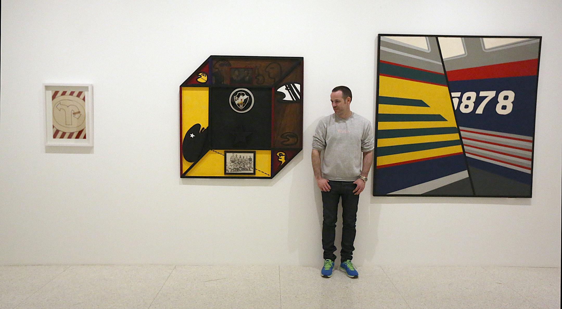 Walker Art Center curator Bart Ryan with three pieces (l to r): Seta machucada (Bruised Arrow)1968 (goauche on paper) by Marcelo Nitsche Brazilian, born 1942; A Familia dividida - Vasco/Botafogo (Divided Family-Vasco/Botafogo) 1968 (painted wood) by Rubens Gerchman Brazilian, 1942-2008; and Lateral de �nibus (Side of the Bus) 1969 (industrial paint on metal) by Raymundo Colares Brazilian, 1944-1986.